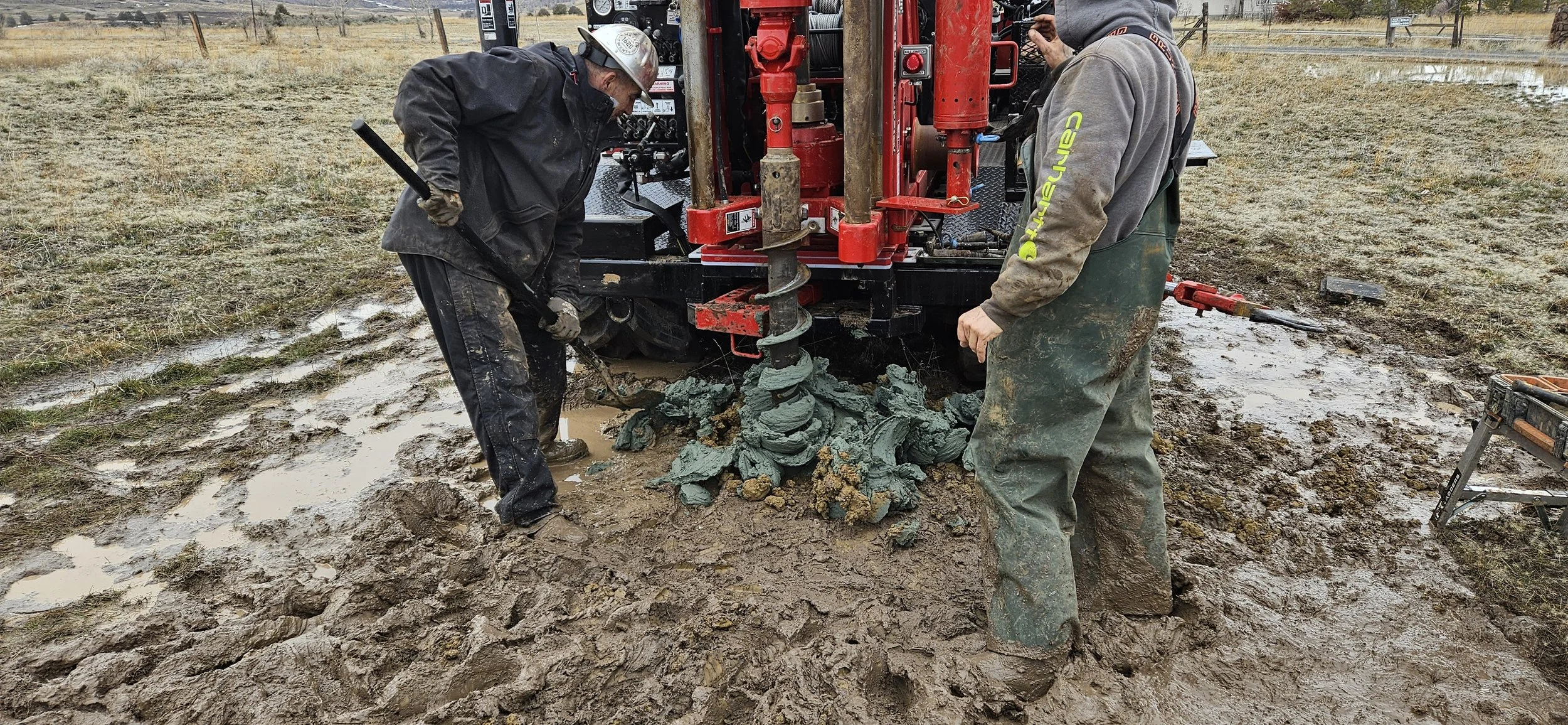 Workers using an auger digger on muddy field for drilling or construction