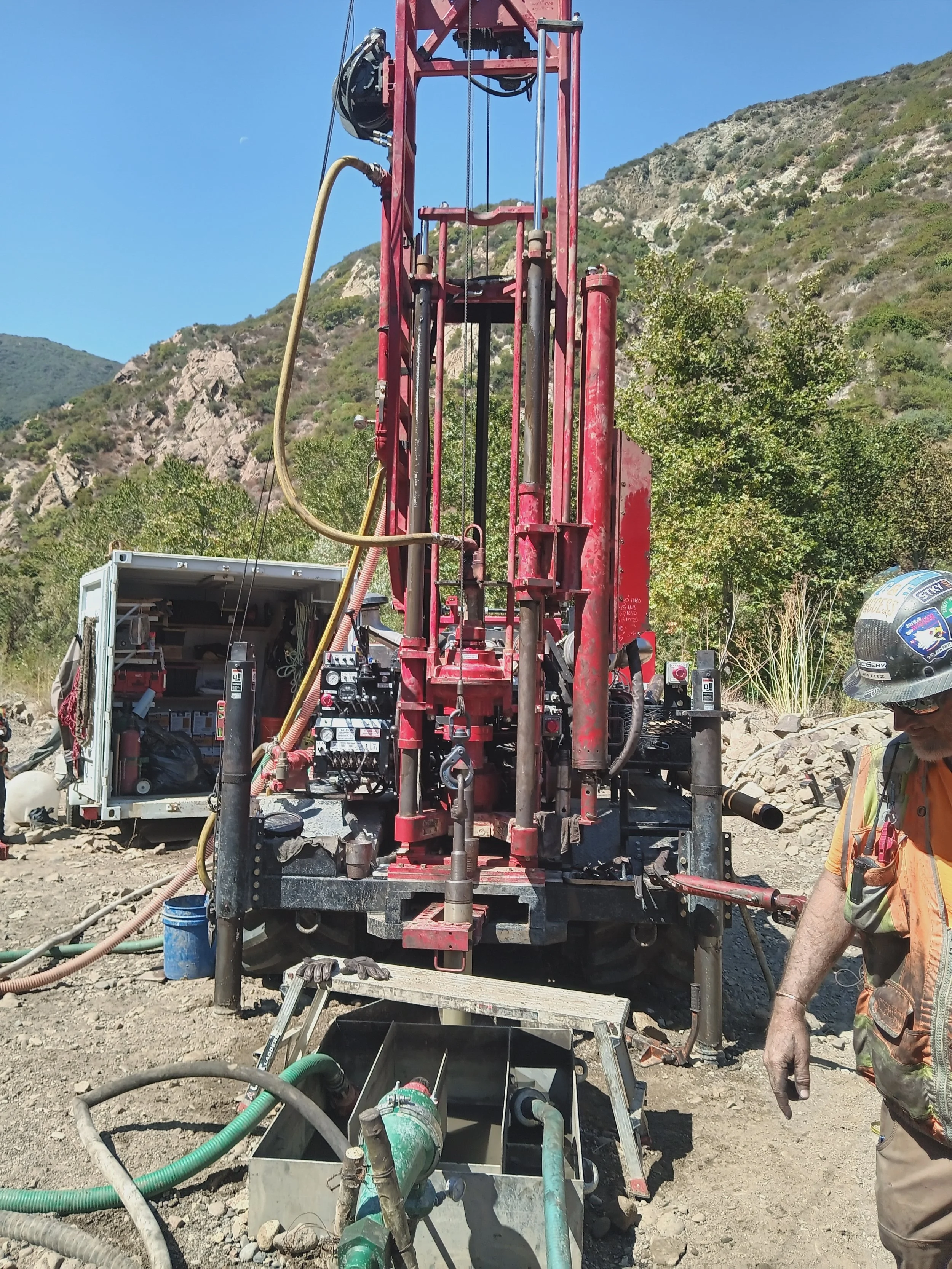Drilling rig on a construction site in a mountainous area with a worker in safety gear nearby