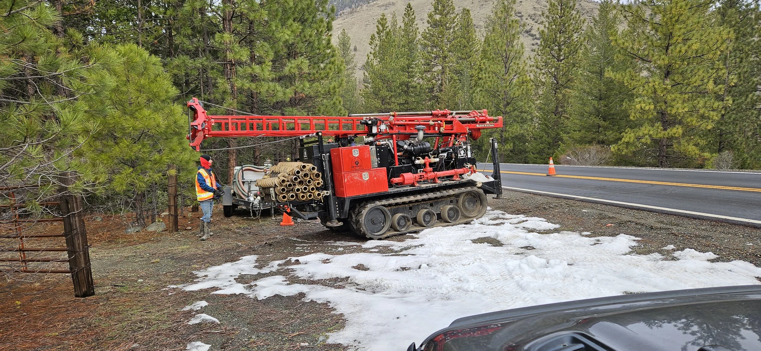 Tracked drill rig near a road with snow and trees