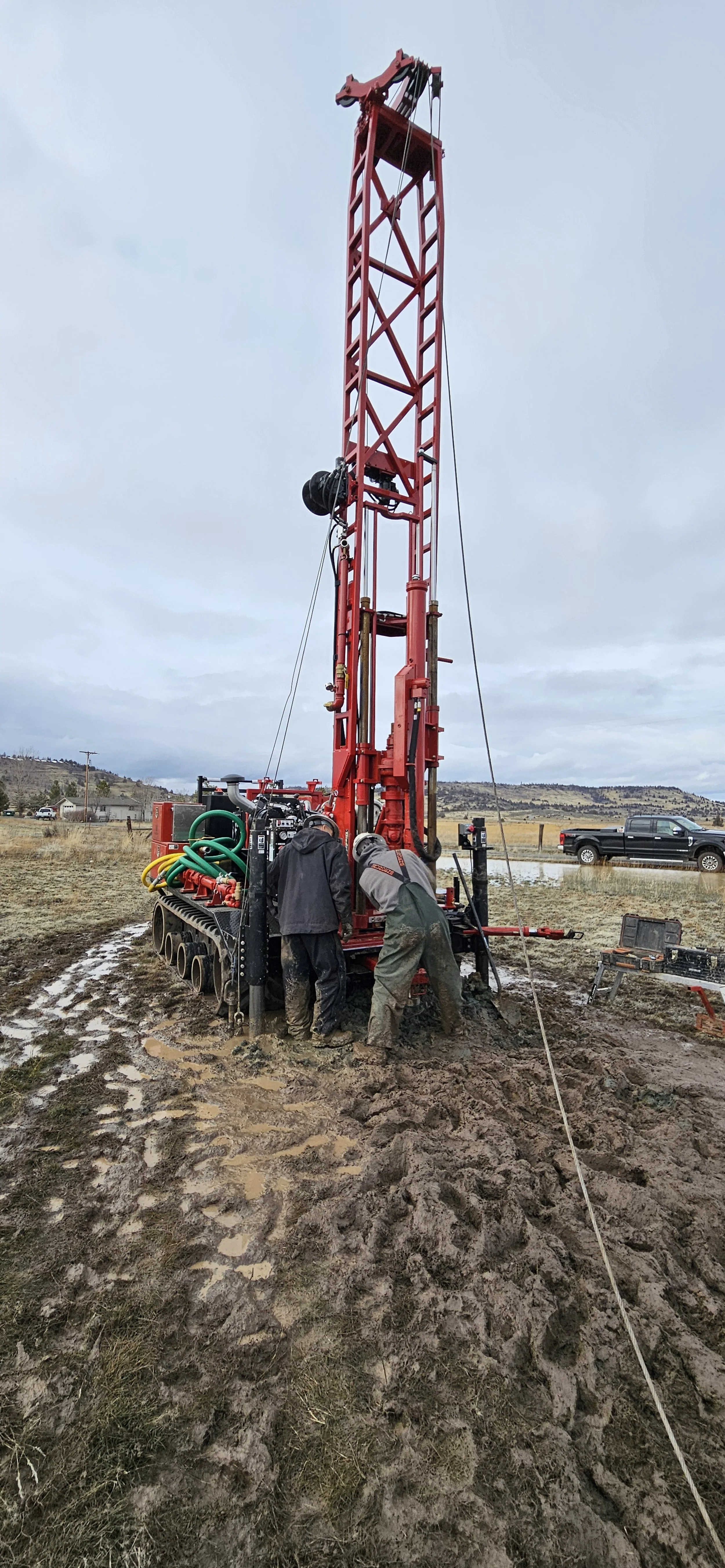 Drilling rig operation in muddy terrain with workers