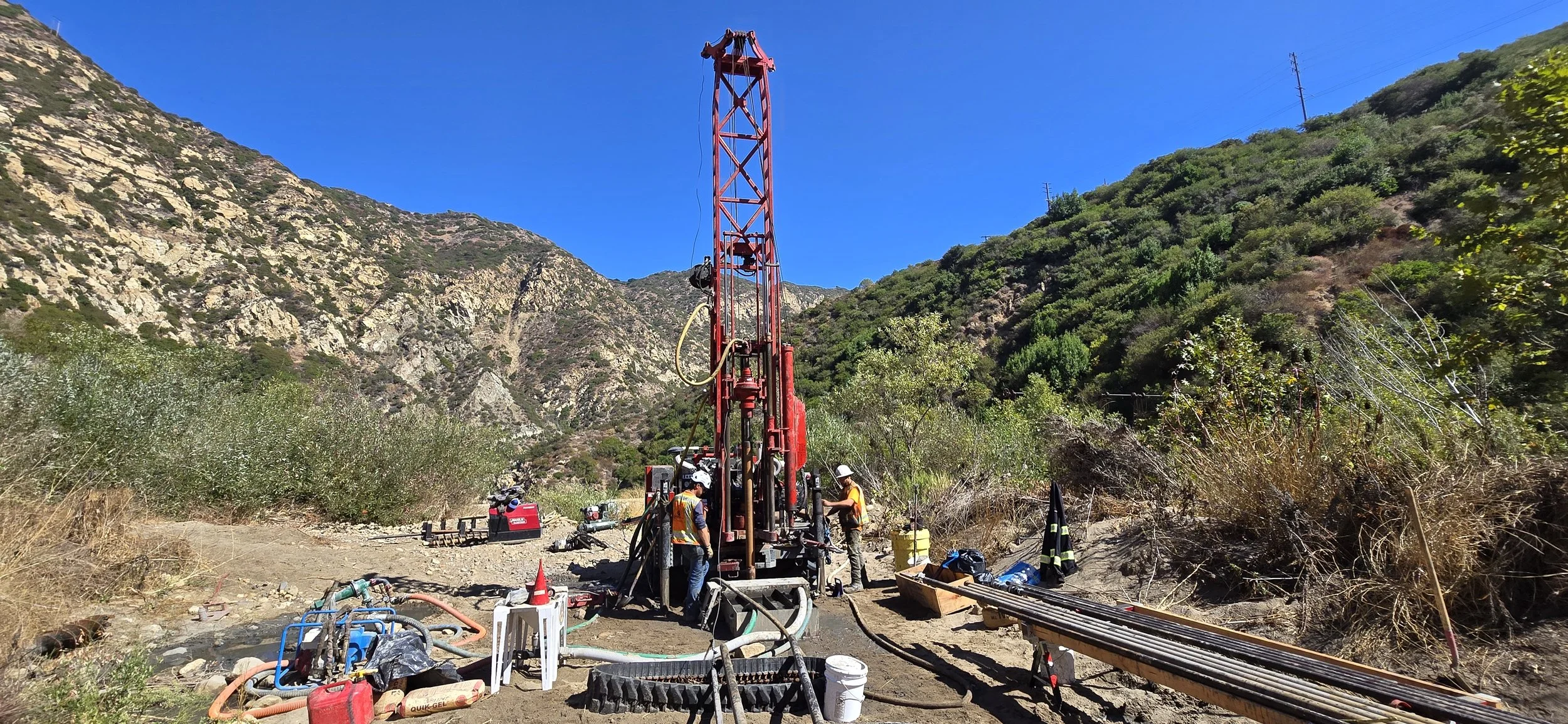 Geological drilling site in mountainous area with red drilling rig and workers