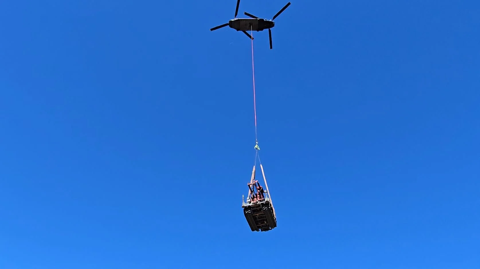 Helicopter lifting equipment with cargo on bright sky background
