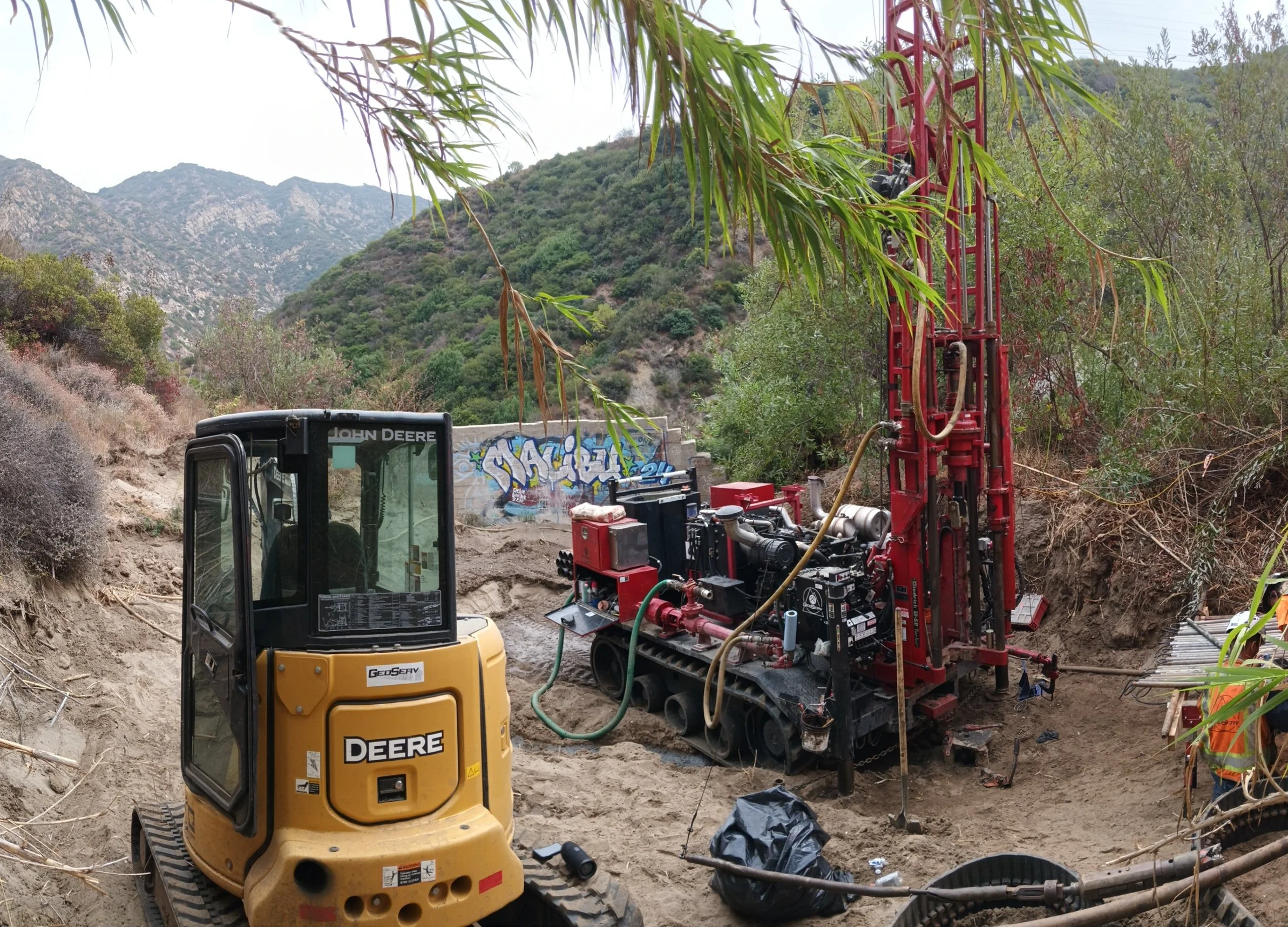 Excavator and drilling rig at construction site in rocky terrain with graffiti on wall