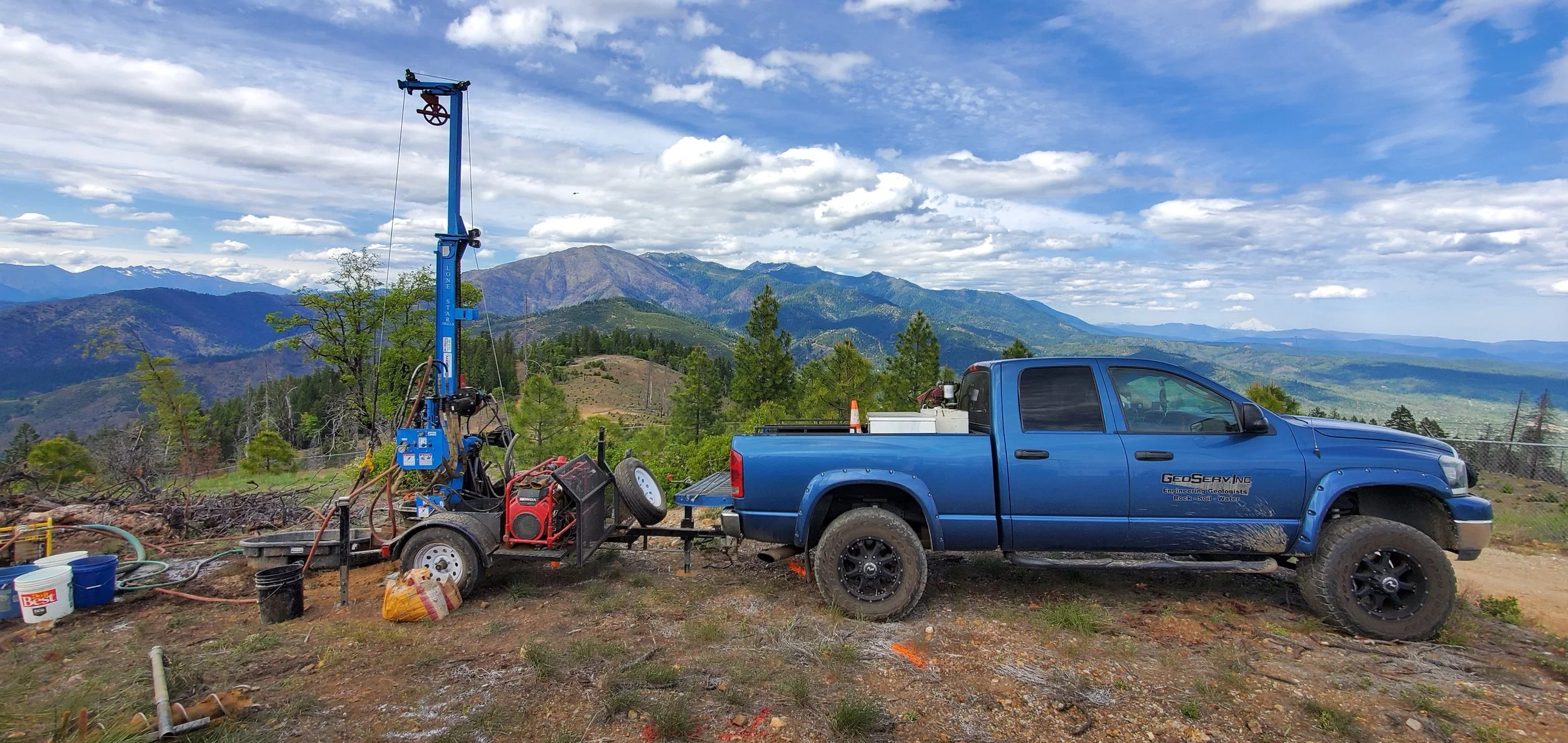 Blue pickup truck with drilling equipment in mountainous landscape