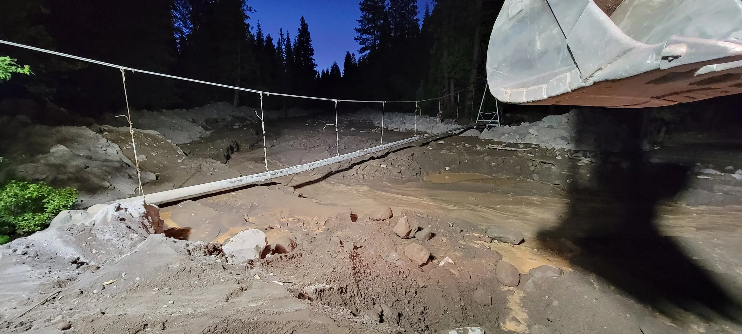 Temporary bridge over muddy terrain with suspended cables at night.