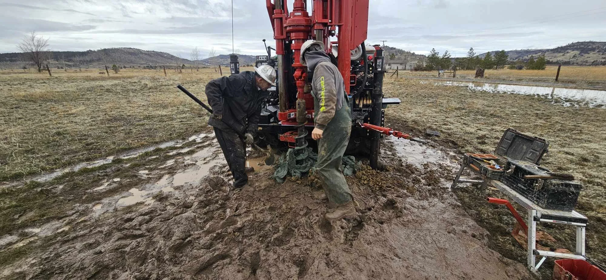 Workers operating a drilling machine in a muddy field