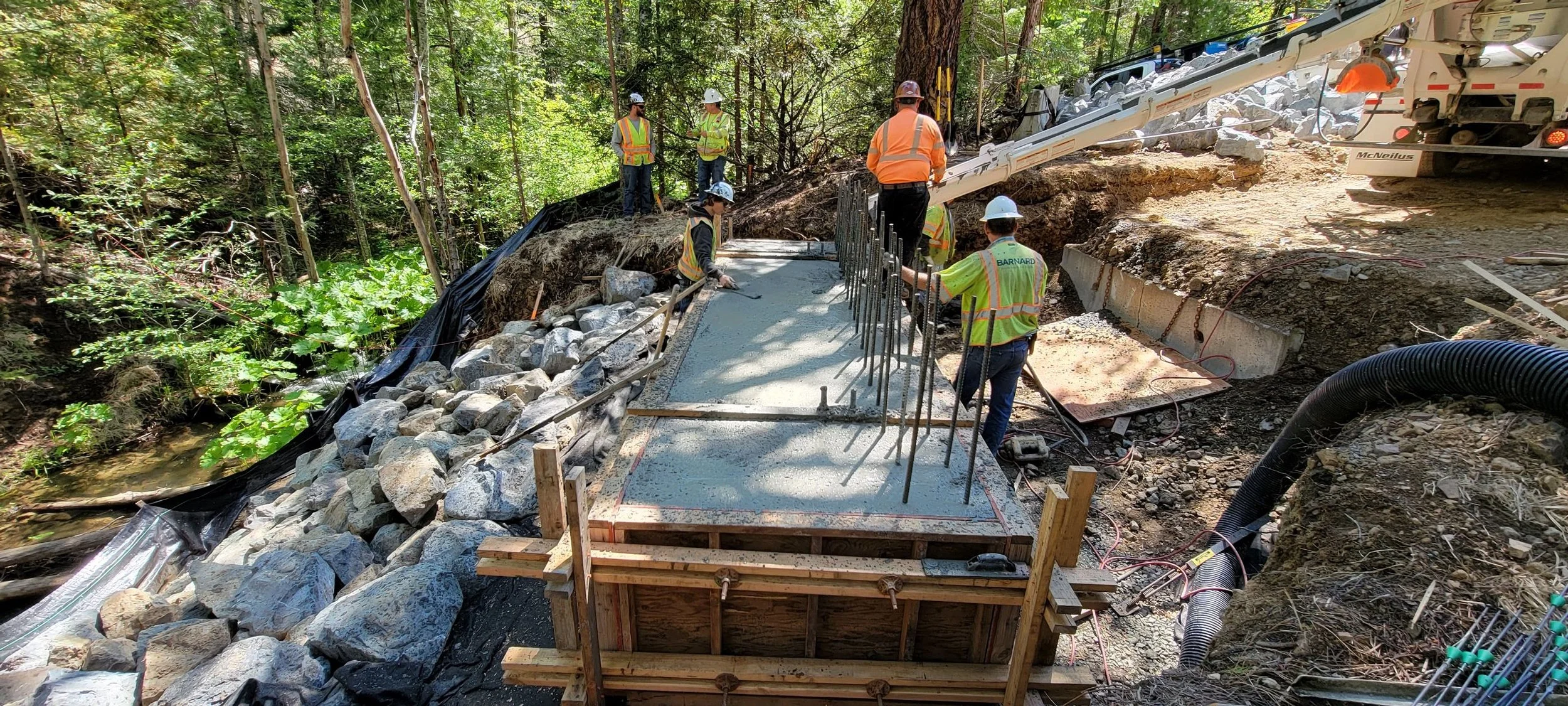 Construction workers pouring concrete for a structure in a forested area