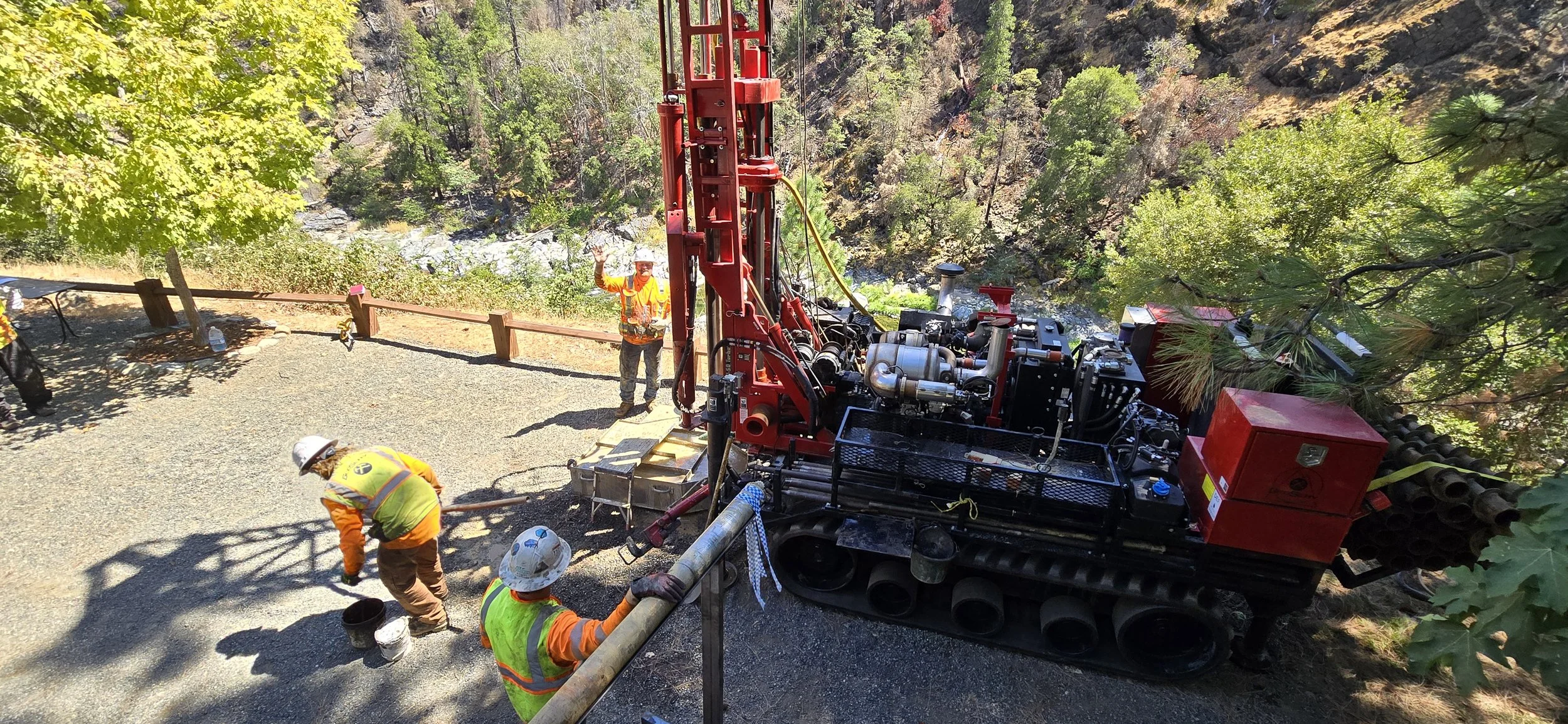 Construction workers operating a drilling rig in a forested area