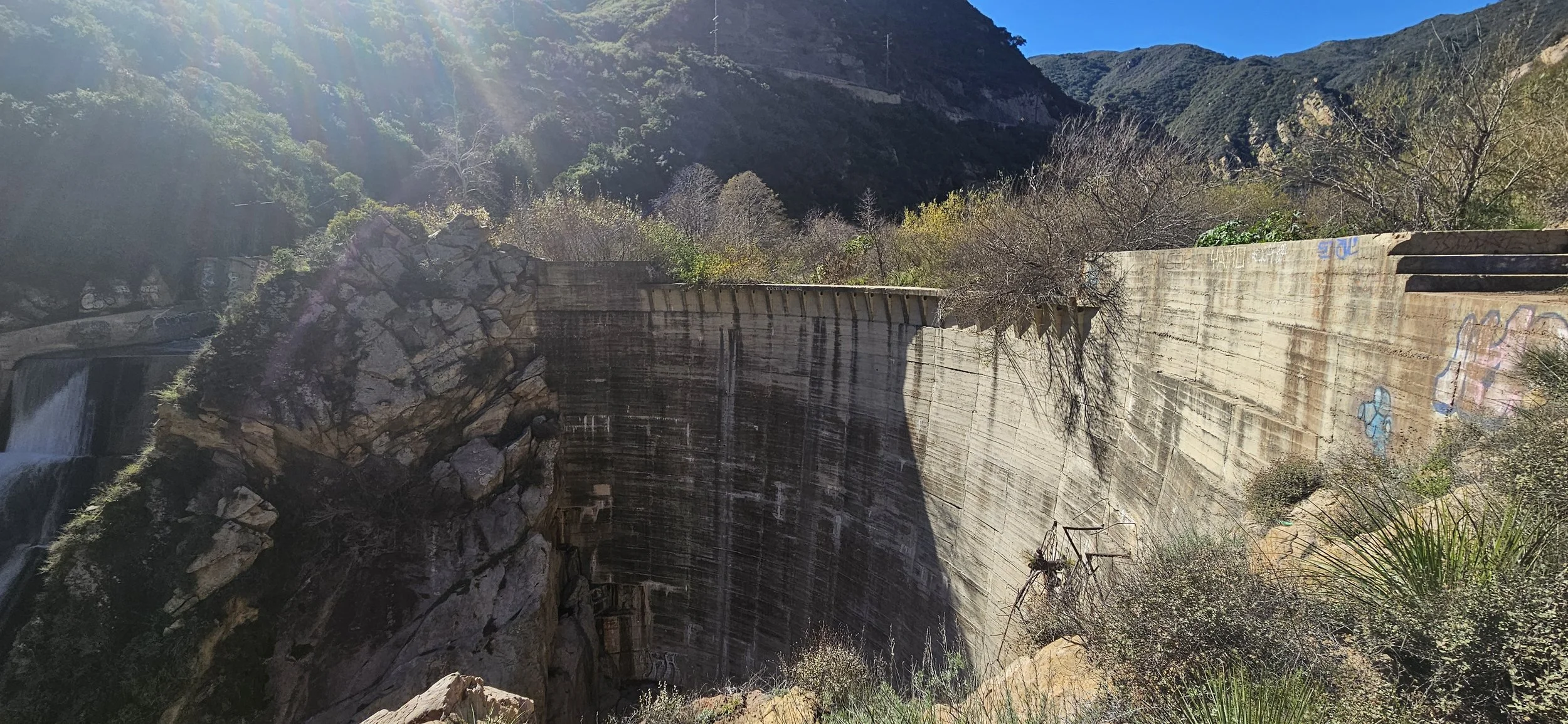 Abandoned dam structure in mountainous area with graffiti and vegetation in foreground
