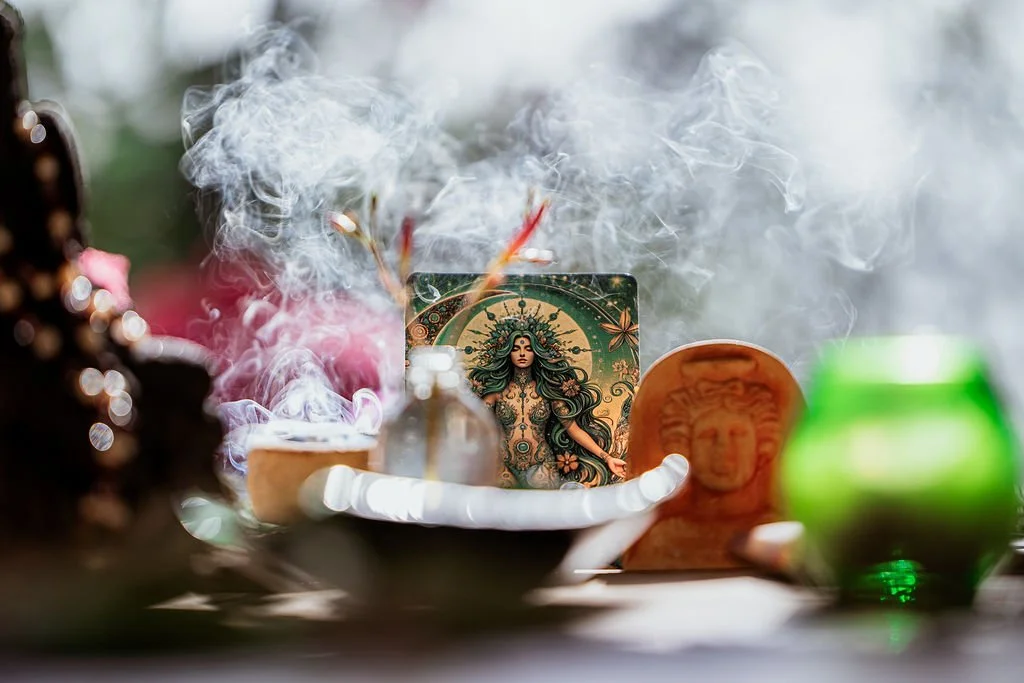 Spiritual altar with candles, incense, and a card featuring a woman with long hair and ornate jewelry, surrounded by smoke and various decorative objects.