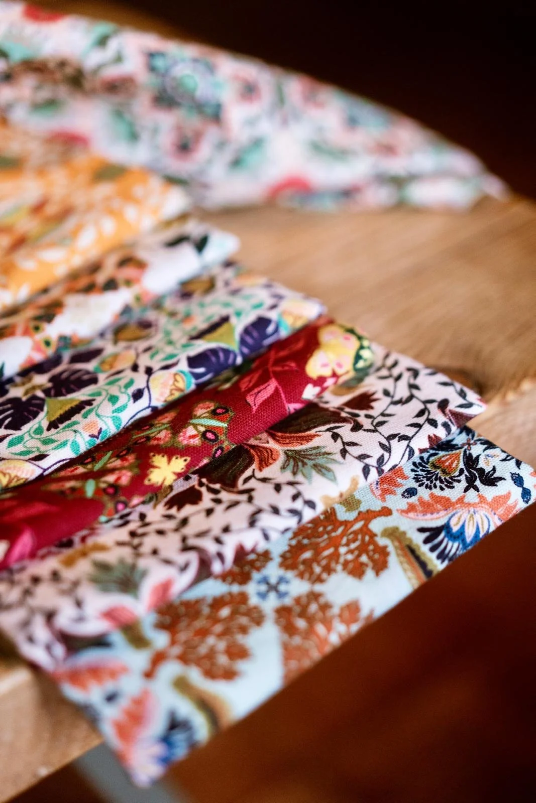 A close-up of colorful folded fabric with floral and intricate patterns laid on a wooden surface.