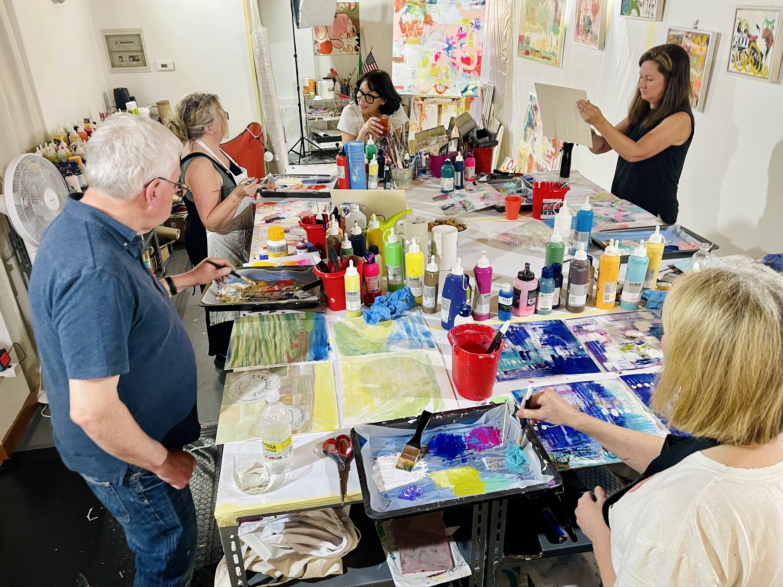 Group of people participating in an art class in Italy with paints, brushes, and colorful paintings on tables and walls.