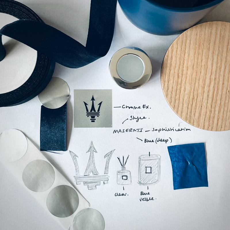 A sketch and mood board featuring Maserati-inspired design elements, including chrome finishes, blue color palette, architectural details, and various material samples such as wood, fabric, and metallic swatches.