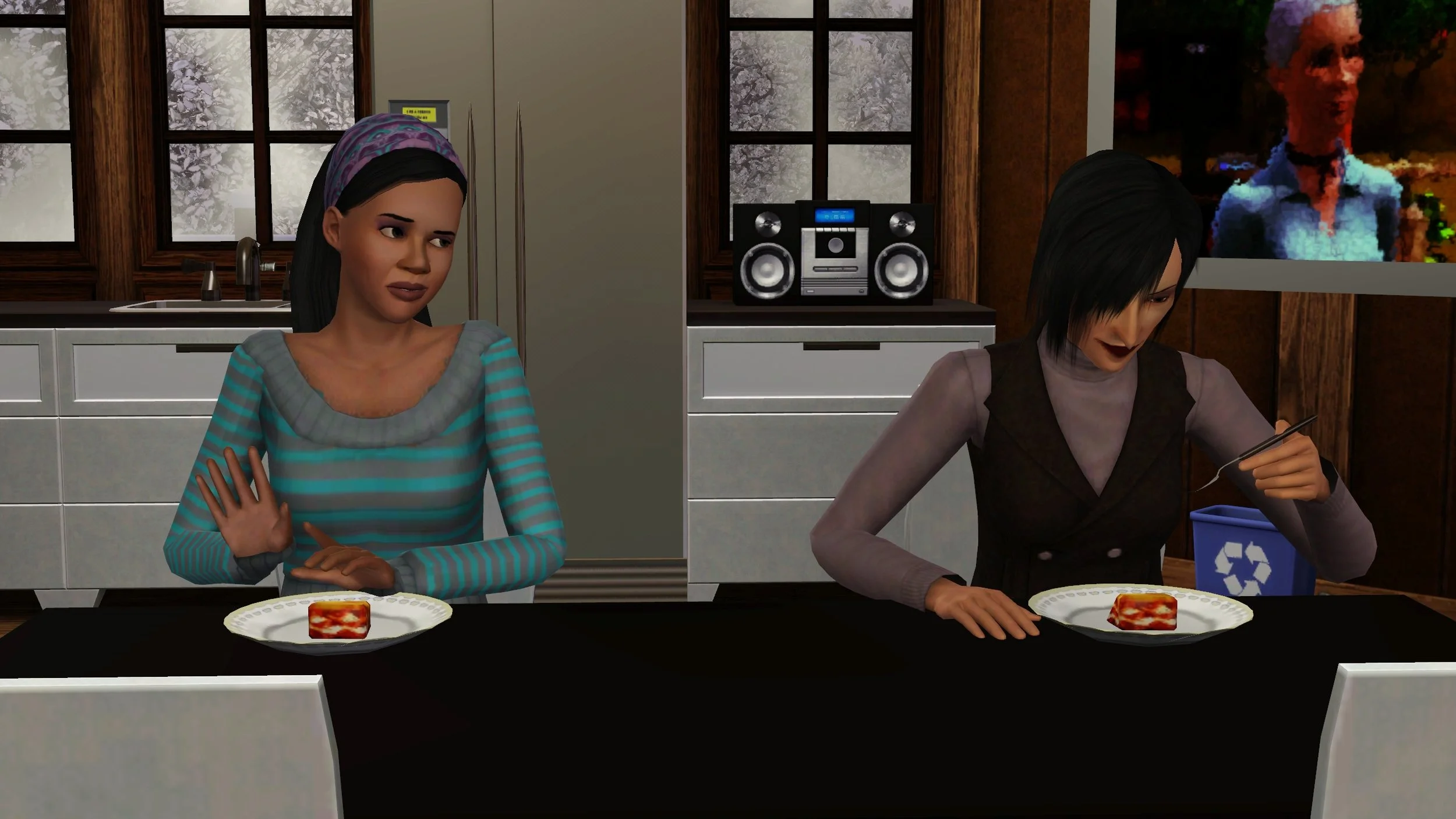 Emery looks at Colette sitting next to her at a dining table with an eyebrow and hands slightly raised. They both have plates of lasagna in front of them; Colette is looking at her fork, halfway to her plate.