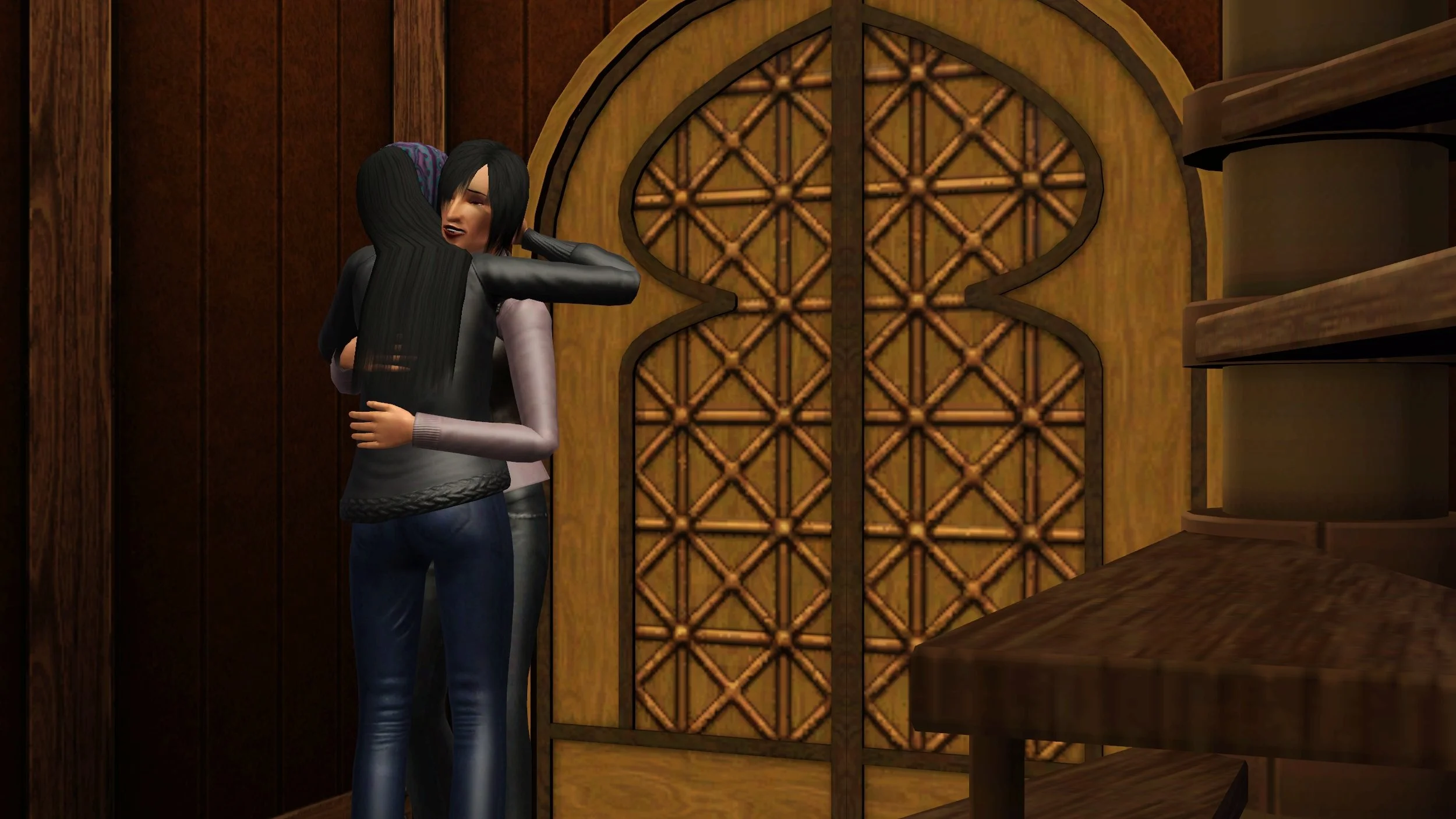 Emery and Colette hug tightly, Emery with one hand behind Colette’s head and Colette’s hands both on Emery’s back. They stand near an ornate wooden door; the camera is positioned near a step of a spiral staircase a few feet away.