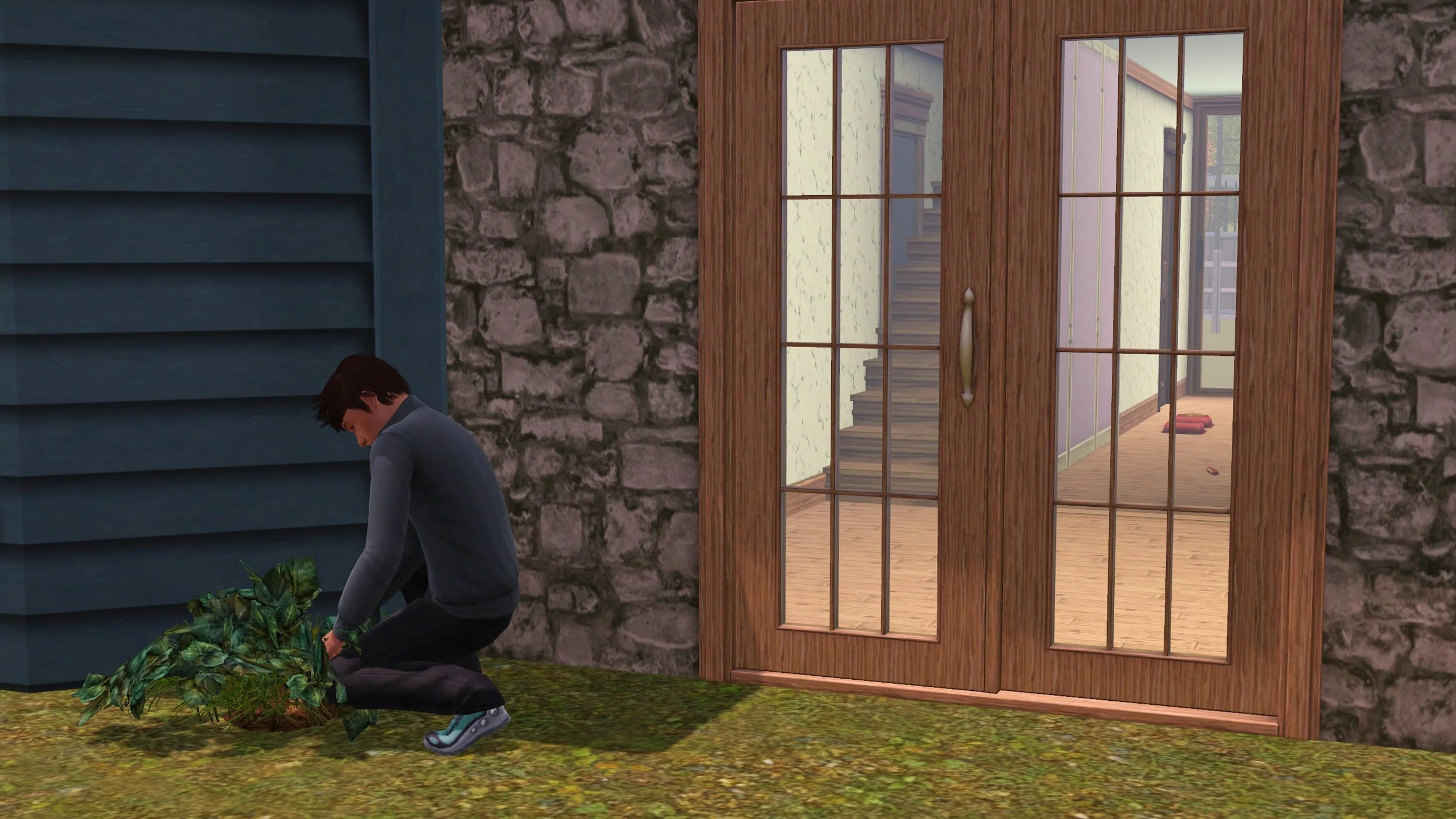 Matthew weeds a plant near his home’s glass front door; through the glass there’s a new staircase blocking a door on one side, a wood framed wall with pink insulation on the side along the arch from the entrance to the kitchen.