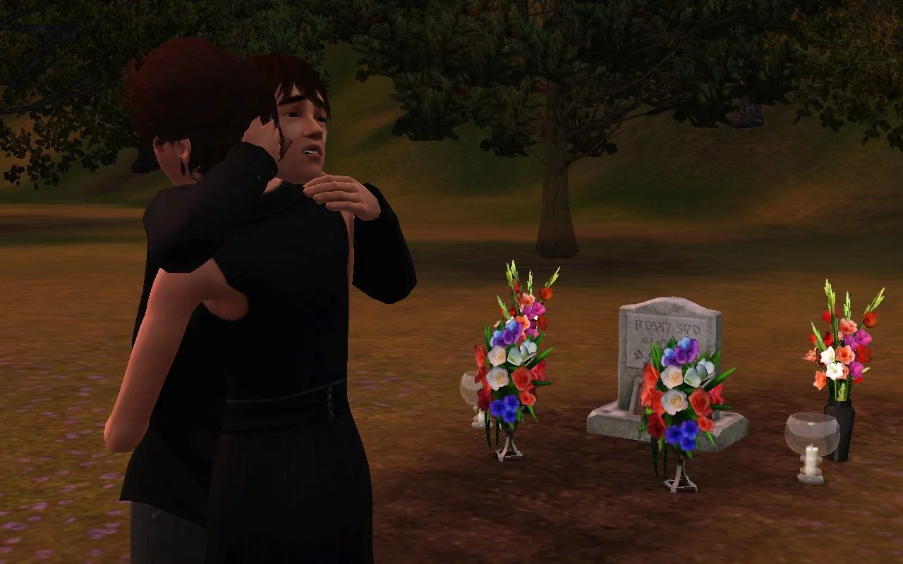 Chase holds Aria's head and shoulder in a hug, a sympathetic or compassionate expression on his face. Altman's grave is clear behind them, surrounded in four vases of colourful flowers and two vases with candles.