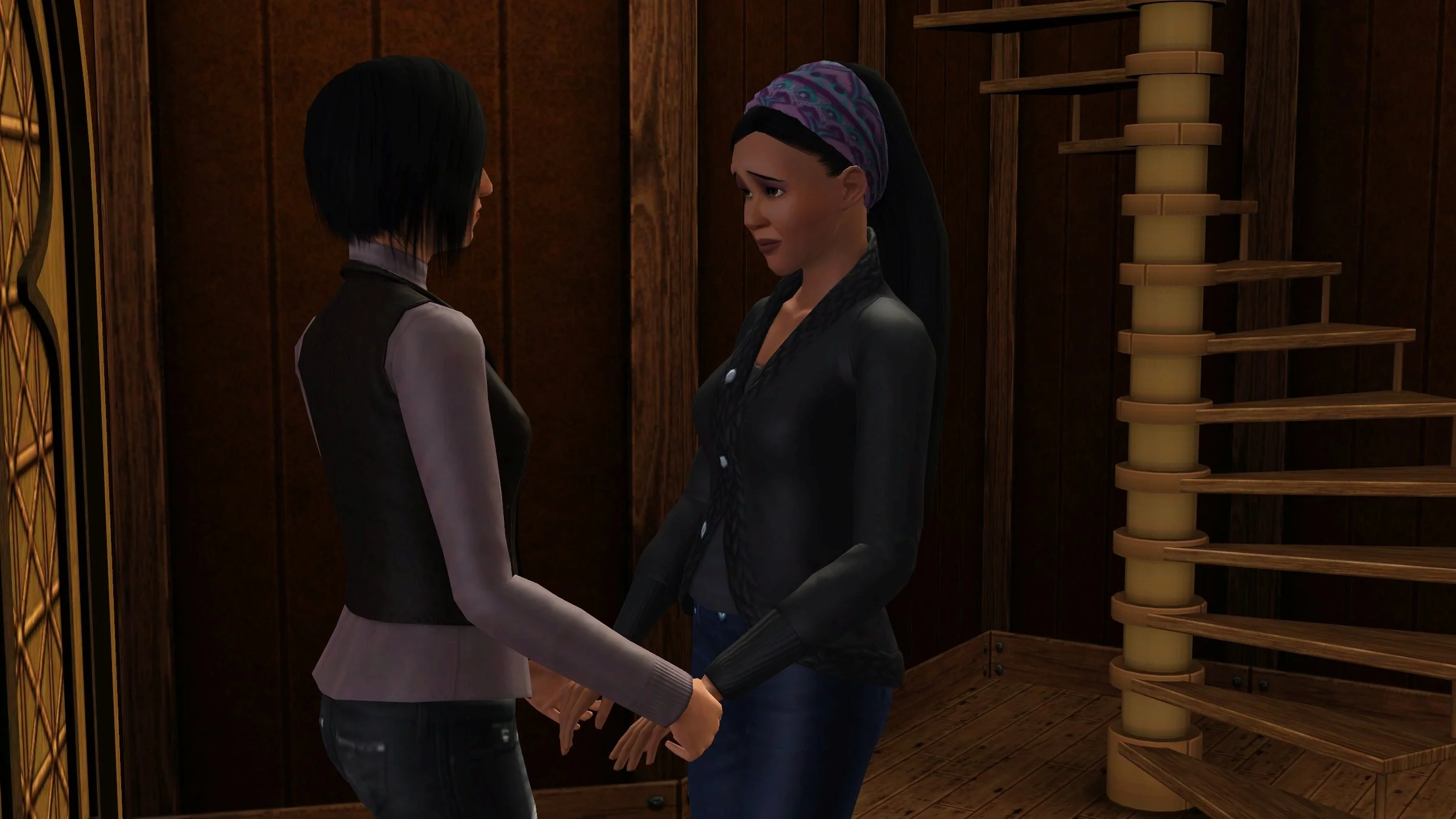 Colette and Emery stand holding hands between an ornate wood door and spiral staircase; Emery’s eyebrows are angled emphasizing the sad look in her eyes and she is frowning slightly.