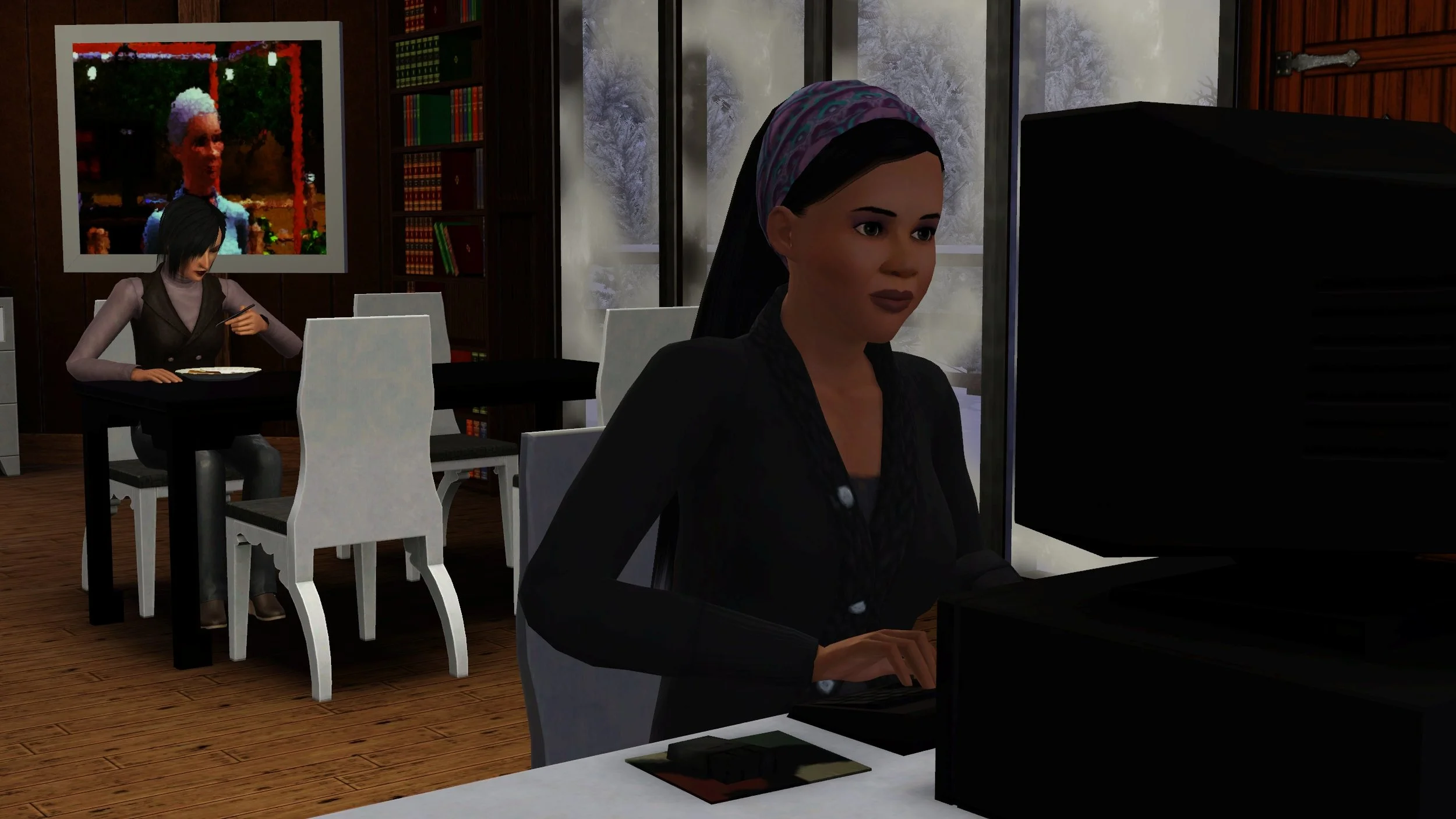 Emery types at her computer desk in the foreground with a neutral expression. Behind her, Colette eats at the dining table next to 4 large frosted windows. In the background is a bookcase and large painting of Emery’s mother.