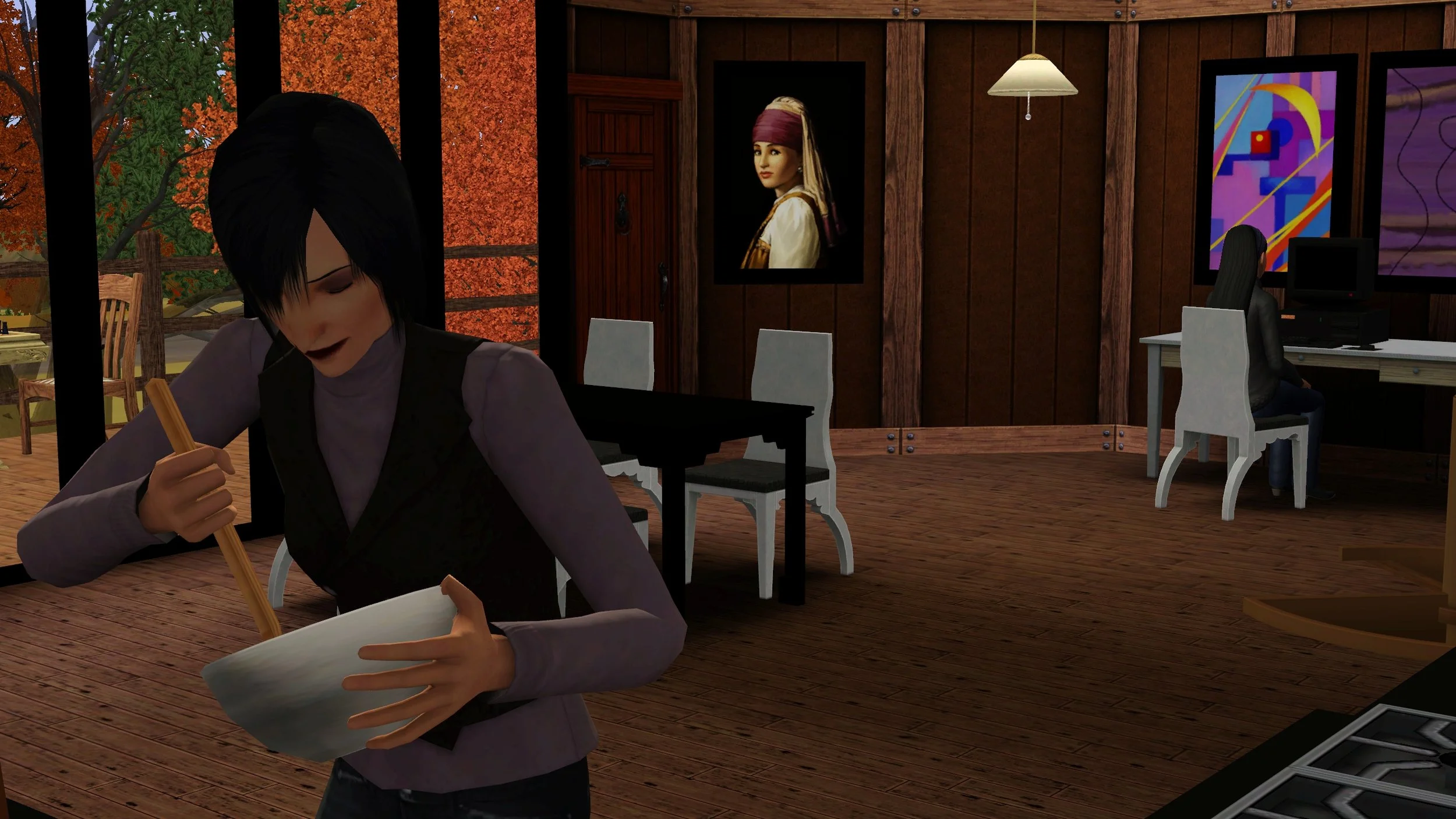 Colette stirs a mixing bowl in the foreground wearing a lilac sweater and brown double-breasted vest. Emery is sitting at her desk in the background but the computer is turned off.