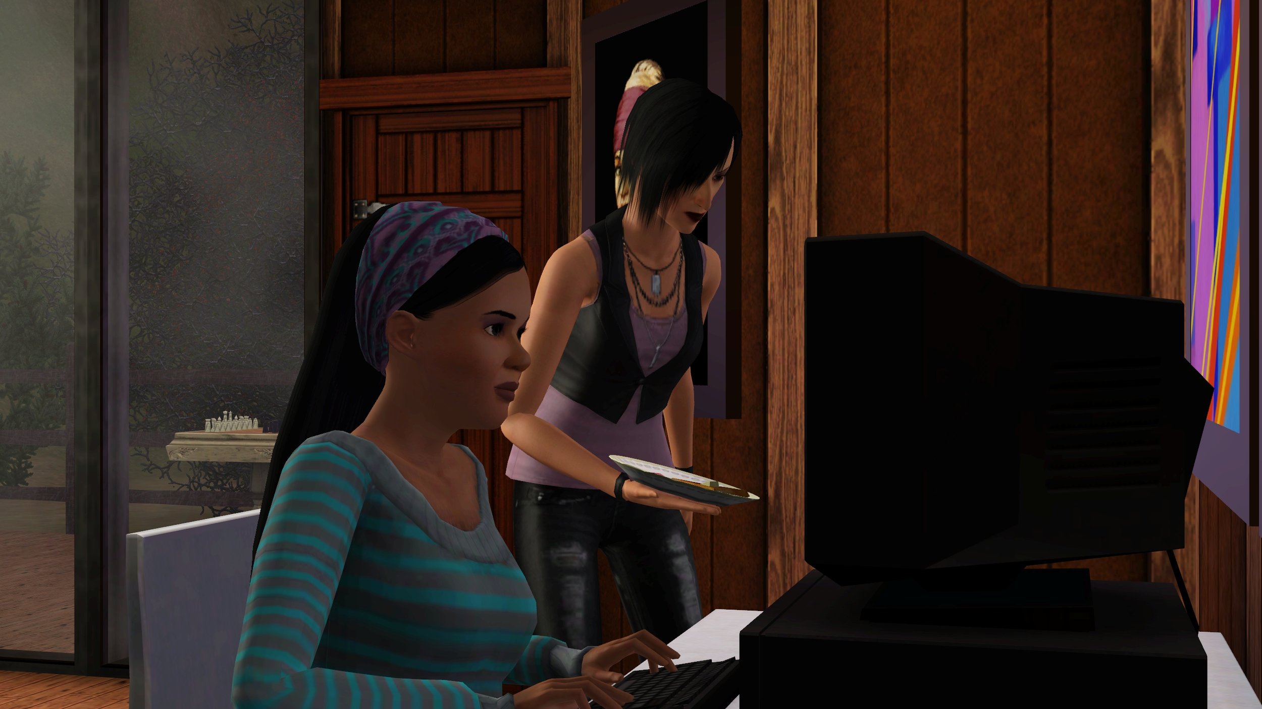 Emery sits typing at her computer, Colette bends to put a plate with a waffle on the desk next to the computer. Behind them are a door to the deck and a window showing the chess table outside, on a cloudy day or early morning light.