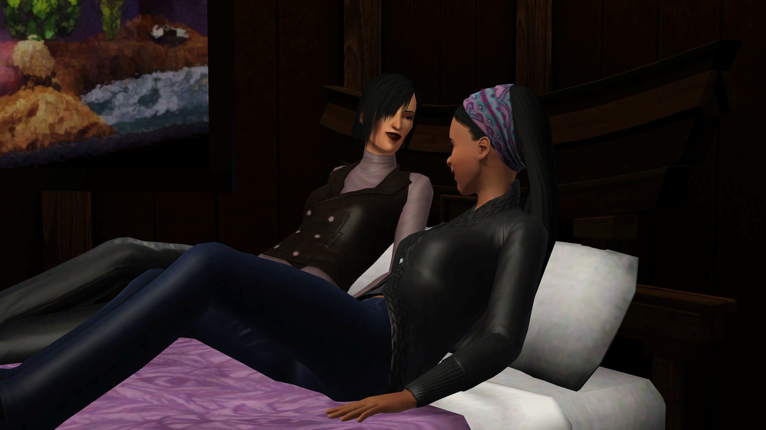 Colette and Emery side-by-side in Emery’s bed, leaning against the headboard. Colette is slightly more upright and looking at Emery, towards the camera; Emery looks towards Colette, with more passive body language. Both wearing jeans and sweaters.