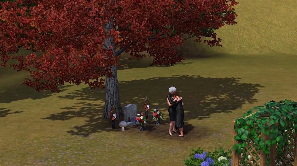 Aria's face against Bridget's shoulder and chest as they embrace in front of Altman's grave. The camera is zoomed out somewhat to show no other Sims nearby. The gravestone is under a tree, surrounded by vases of flowers and candles.