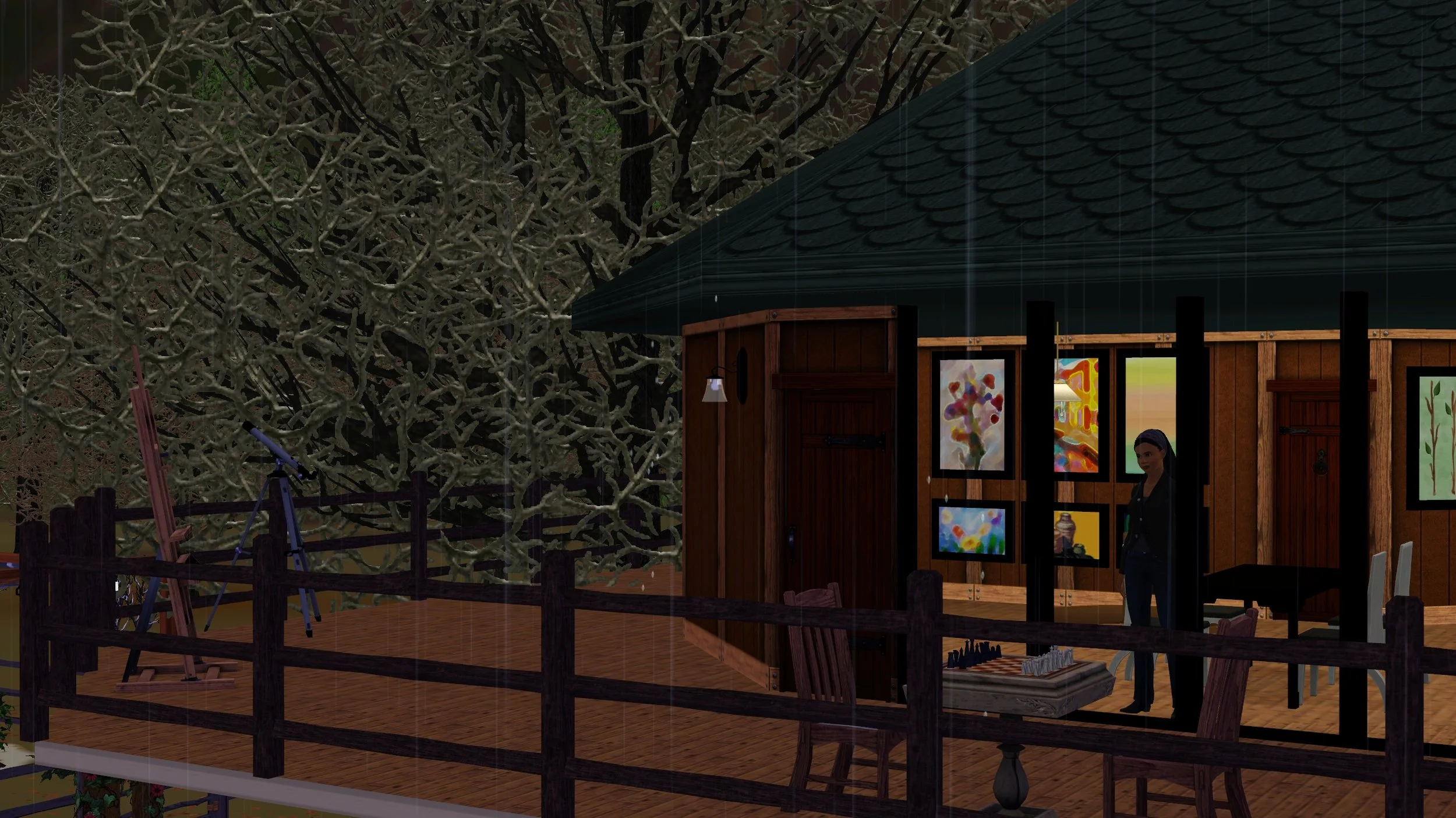 Emery looks out a set of 4 large windows; it’s raining outside, trees’ bare branches are frosted; the large wrap-around deck has a telescope, easel, and chess board with 2 chairs. Inside the house are paintings and a dining table with 4 chairs.