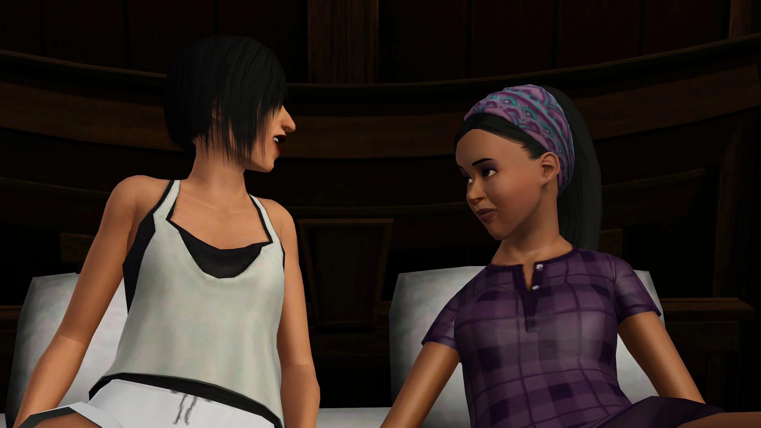 Close-up of Colette and Emery looking at each other, leaning on pillows against a bed’s headboard. Colette holds herself up slightly, wearing a tank top. Emery looks up at her, eyes wide, with her chin angled down, wearing a T-shirt style nightgown.