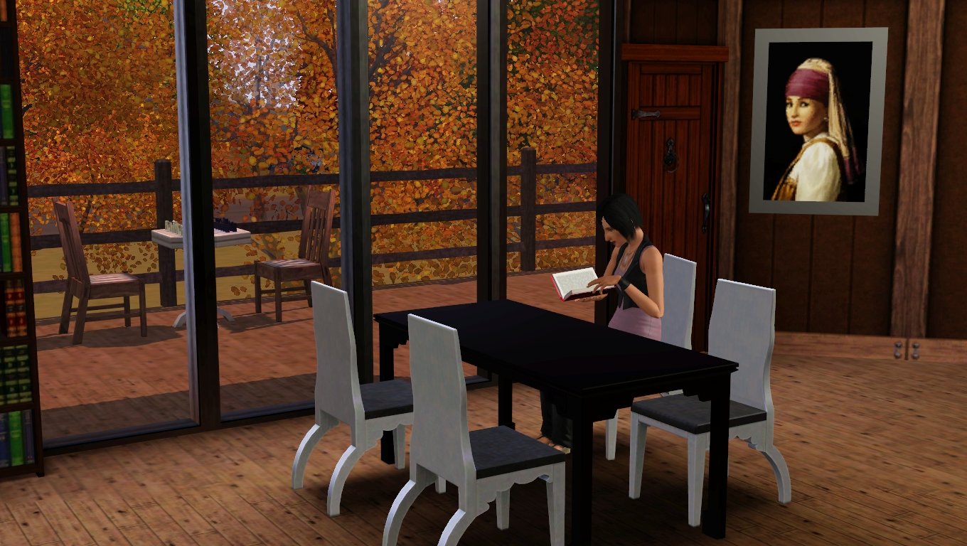 Colette sits reading a book at the dining table wearing a lilac tank top under a cropped black vest. The view through four large windows is filled with orange leaves; a chess table with two chairs is on the deck outside.