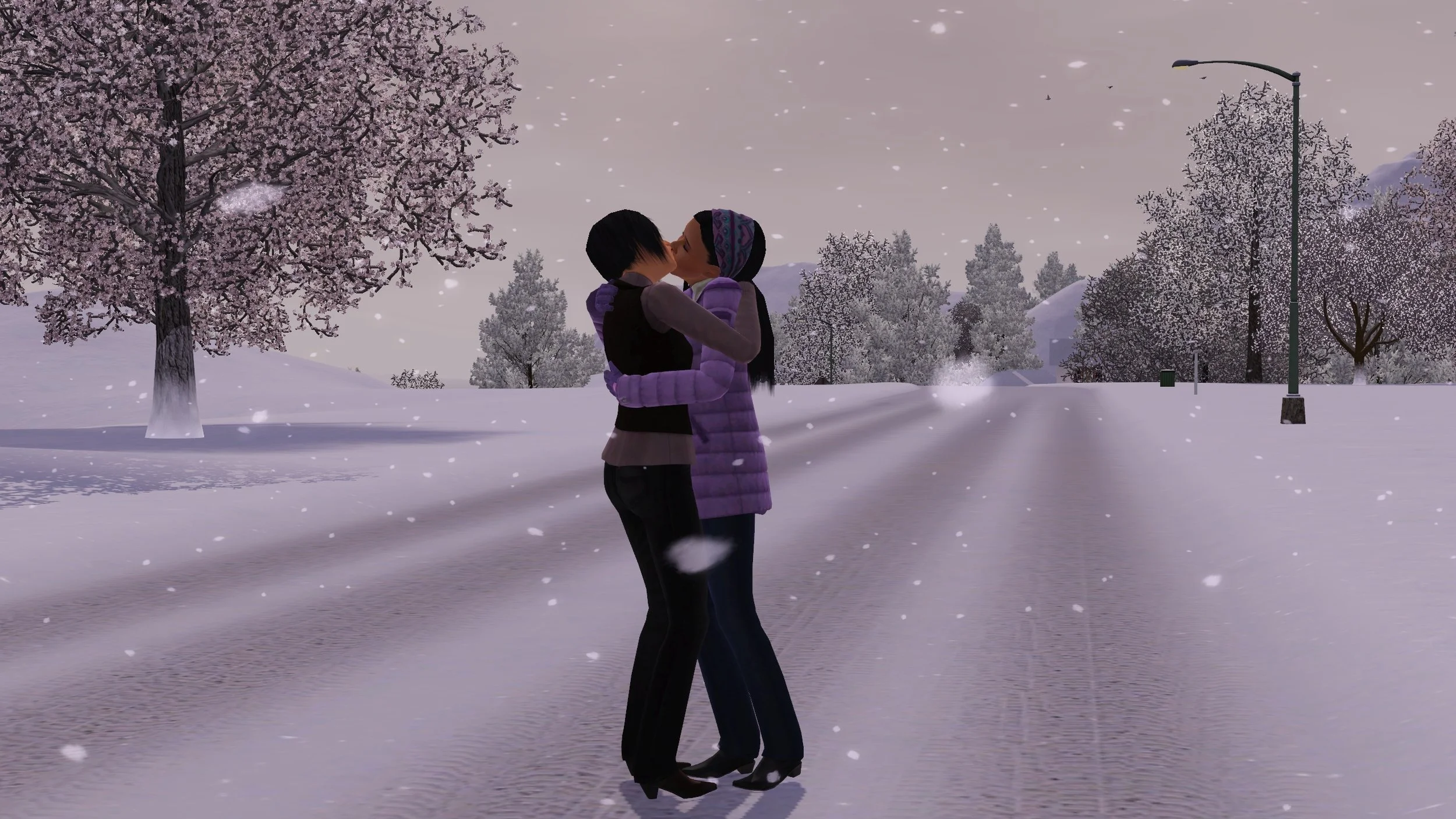 Colette and Emery kiss passionately with their arms around each other, standing in a snow-covered empty street. Large fluffy snowflakes fall around them. Frost-covered bare trees are scattered along the road.