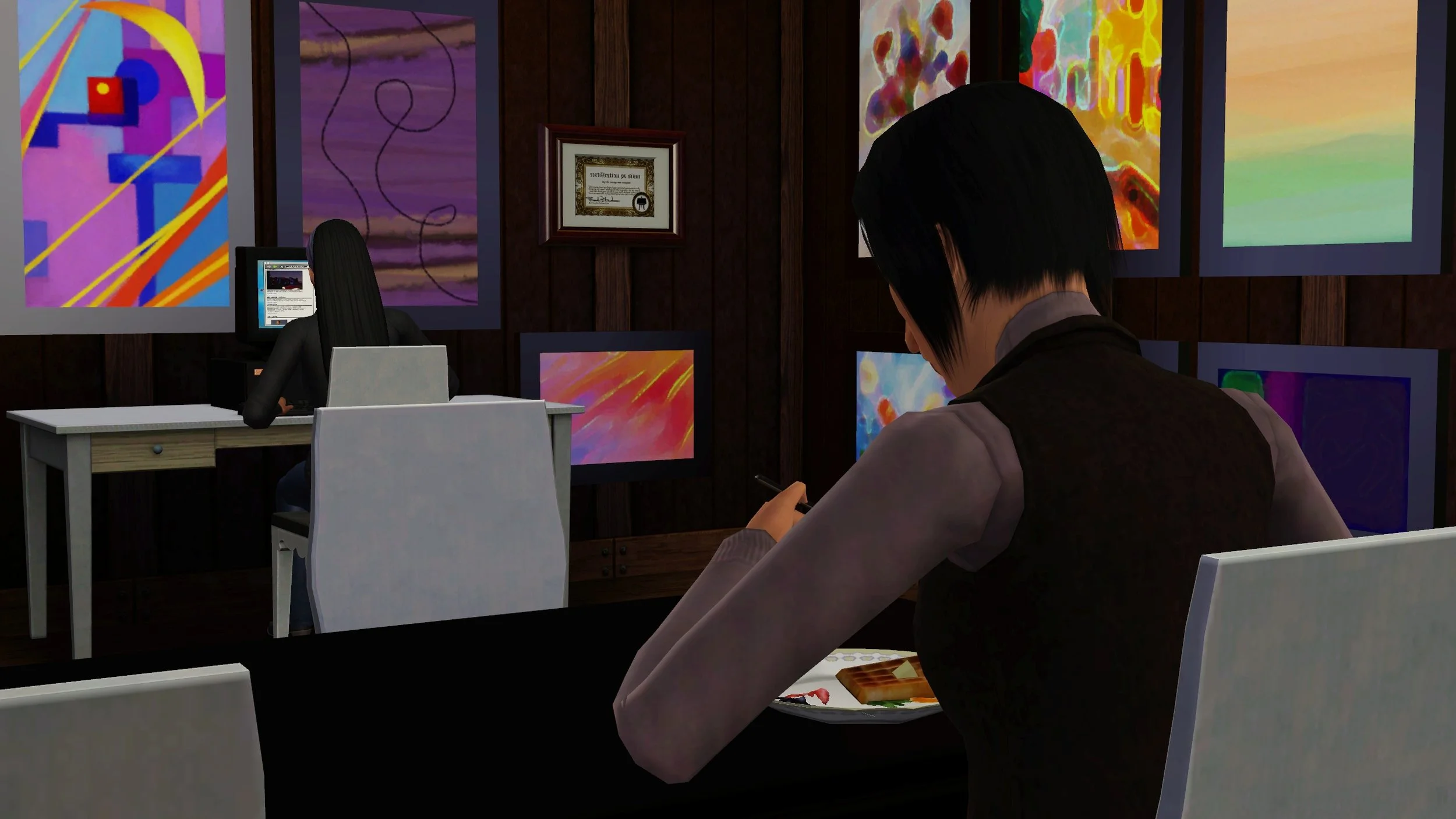 In the foreground, Colette eats a waffle at the dining table facing away from the camera, towards Emery typing at her computer desk, also facing away from the camera. The walls are covered in Emery’s paintings and a painting skill certificate.