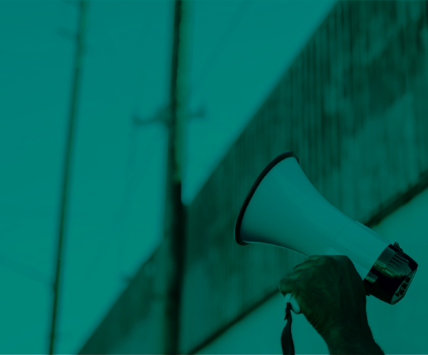 a hand holding a megaphone with a bulding and powerlines in the background. The image has a teal color overlay on it.