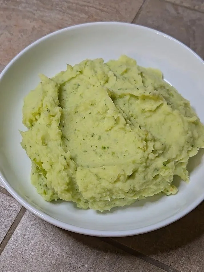 A bowl of mashed potatoes with herbs placed on a tiled surface.