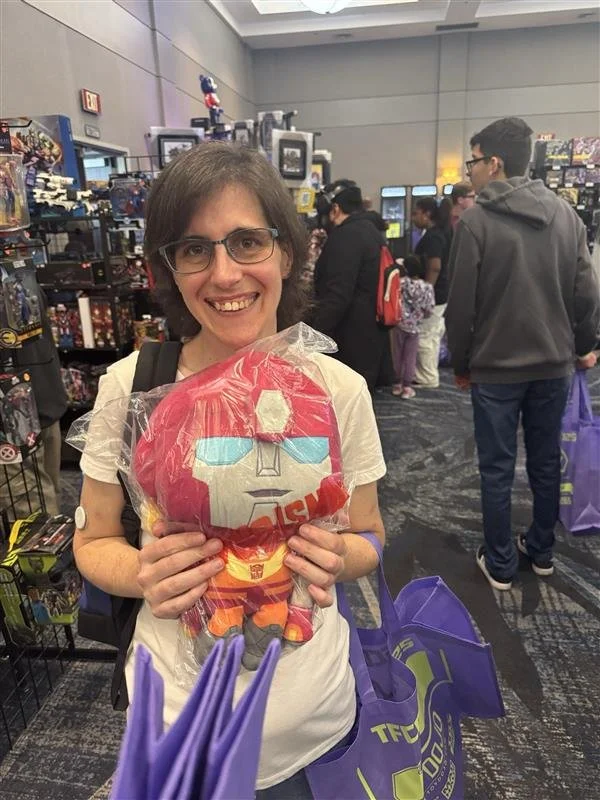 Woman holding a plush toy of Iron Man at a toy or comic convention.
