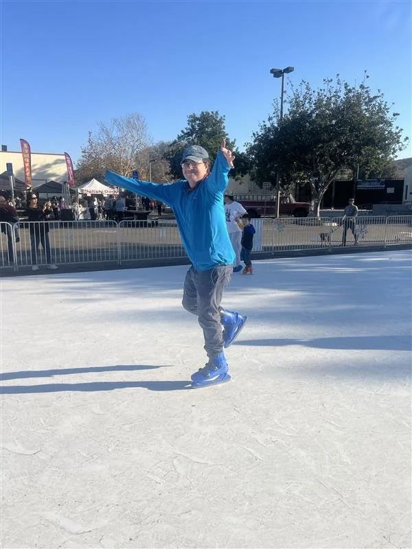 Person ice skating on an outdoor rink, smiling and striking a playful pose.