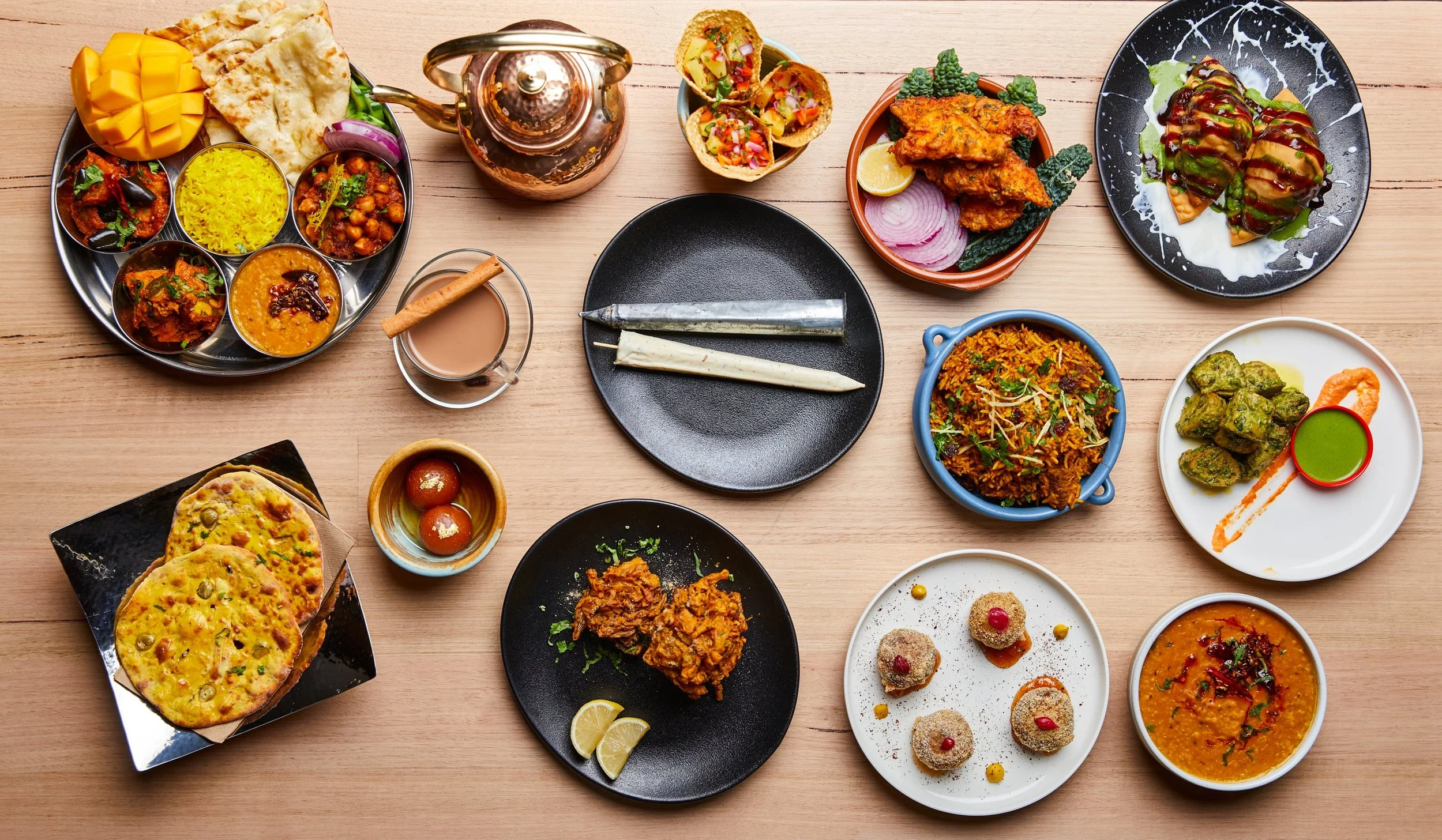 A variety of Indian dishes served on a wooden table, including curries, rice, bread, chutney, and desserts.