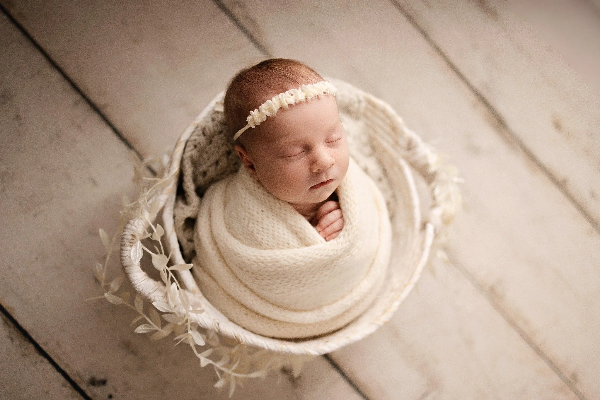 Sleeping newborn in a cream wrap and floral headband in a white woven basket