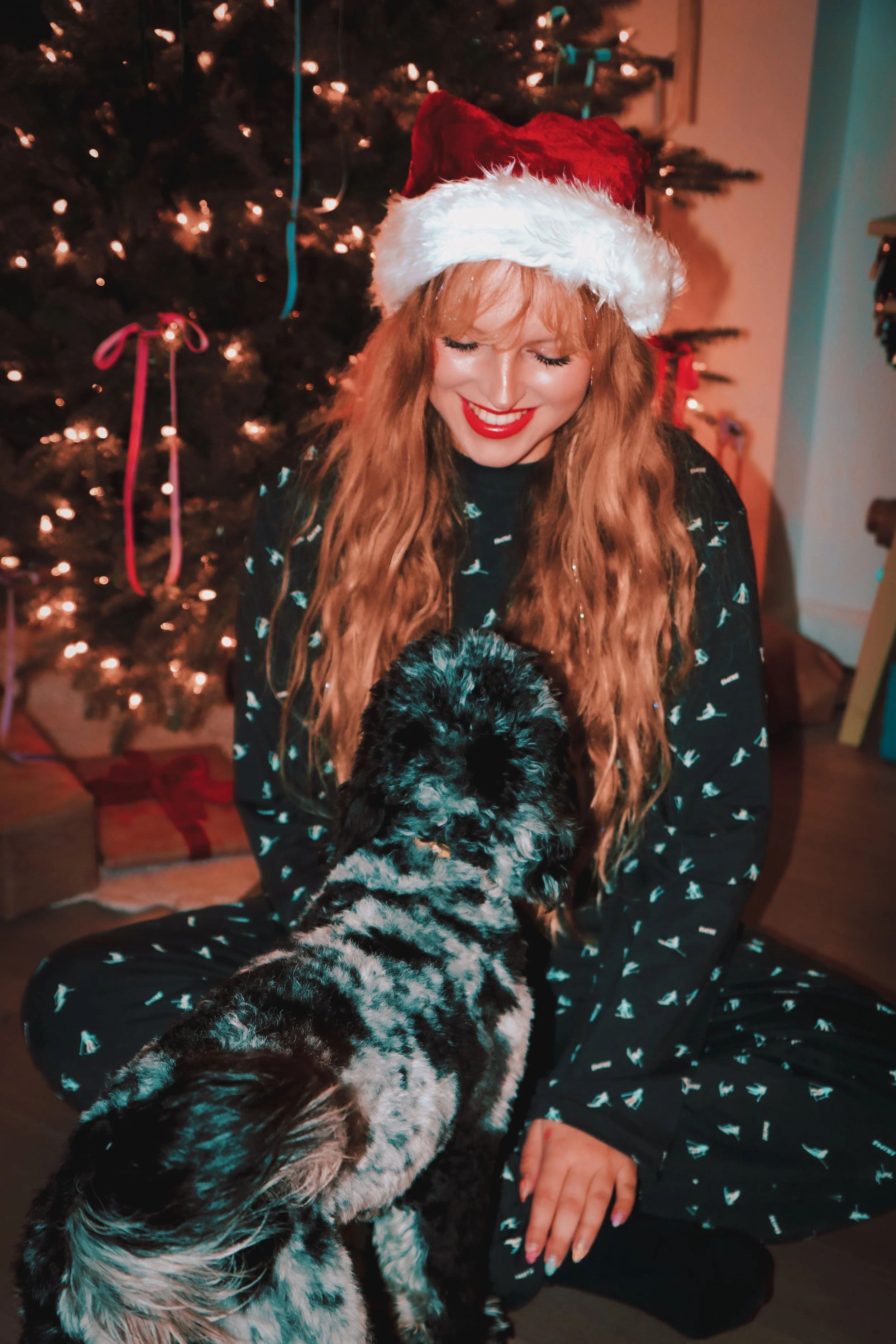 Woman in Santa hat with dog by Christmas tree