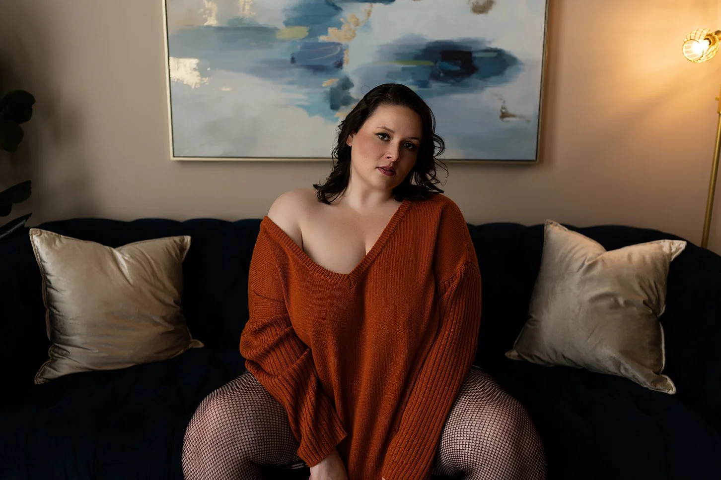 women wearing an orange sweater off the shoulder, sitting on a blue couch with gold pillows