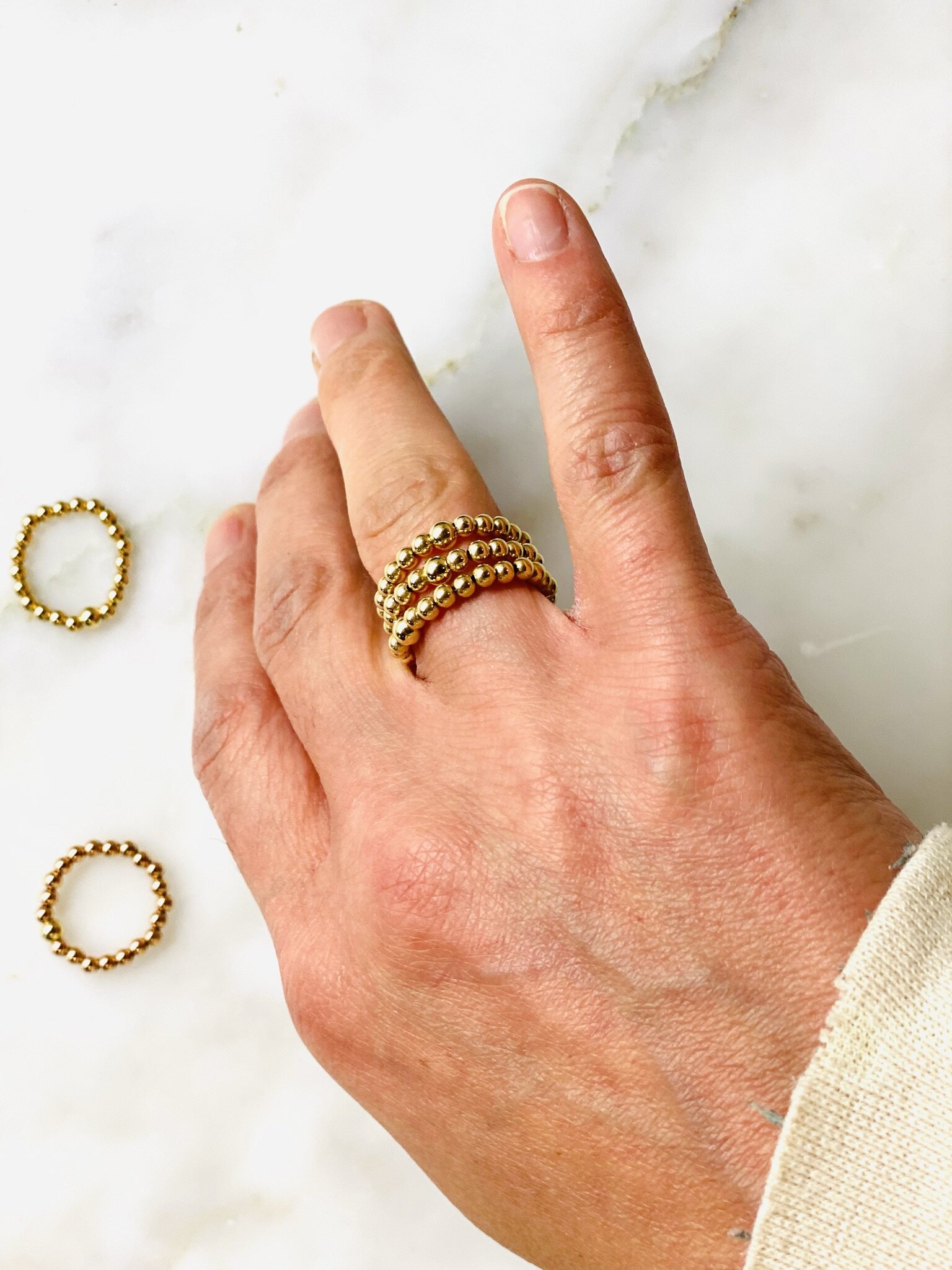 Image of multiple 3mm gold beaded rings on middle finger.