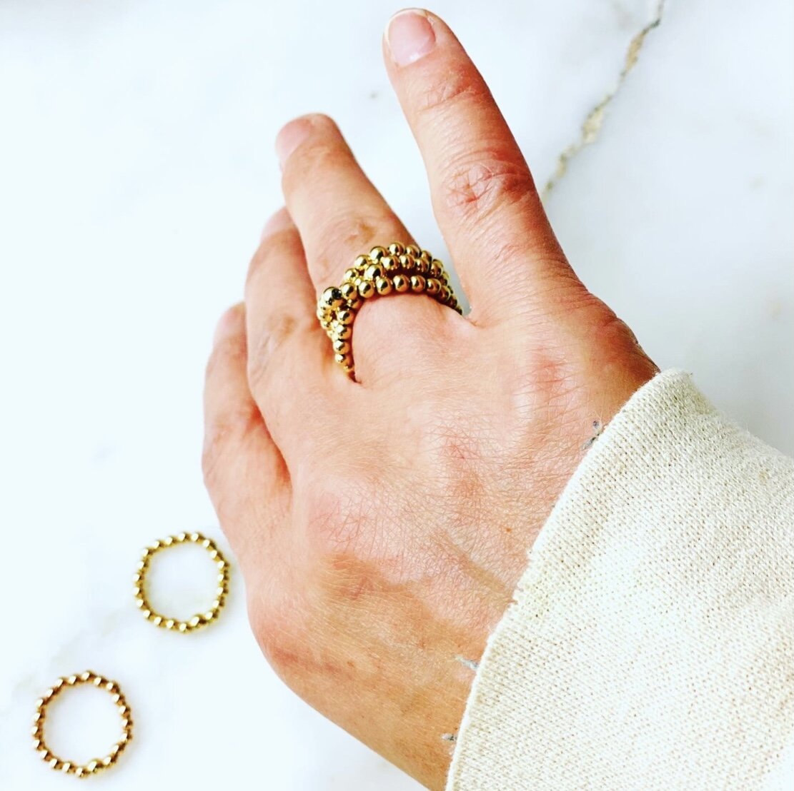 Image of multiple gold beaded 3mm rings on middle finger, twisted.