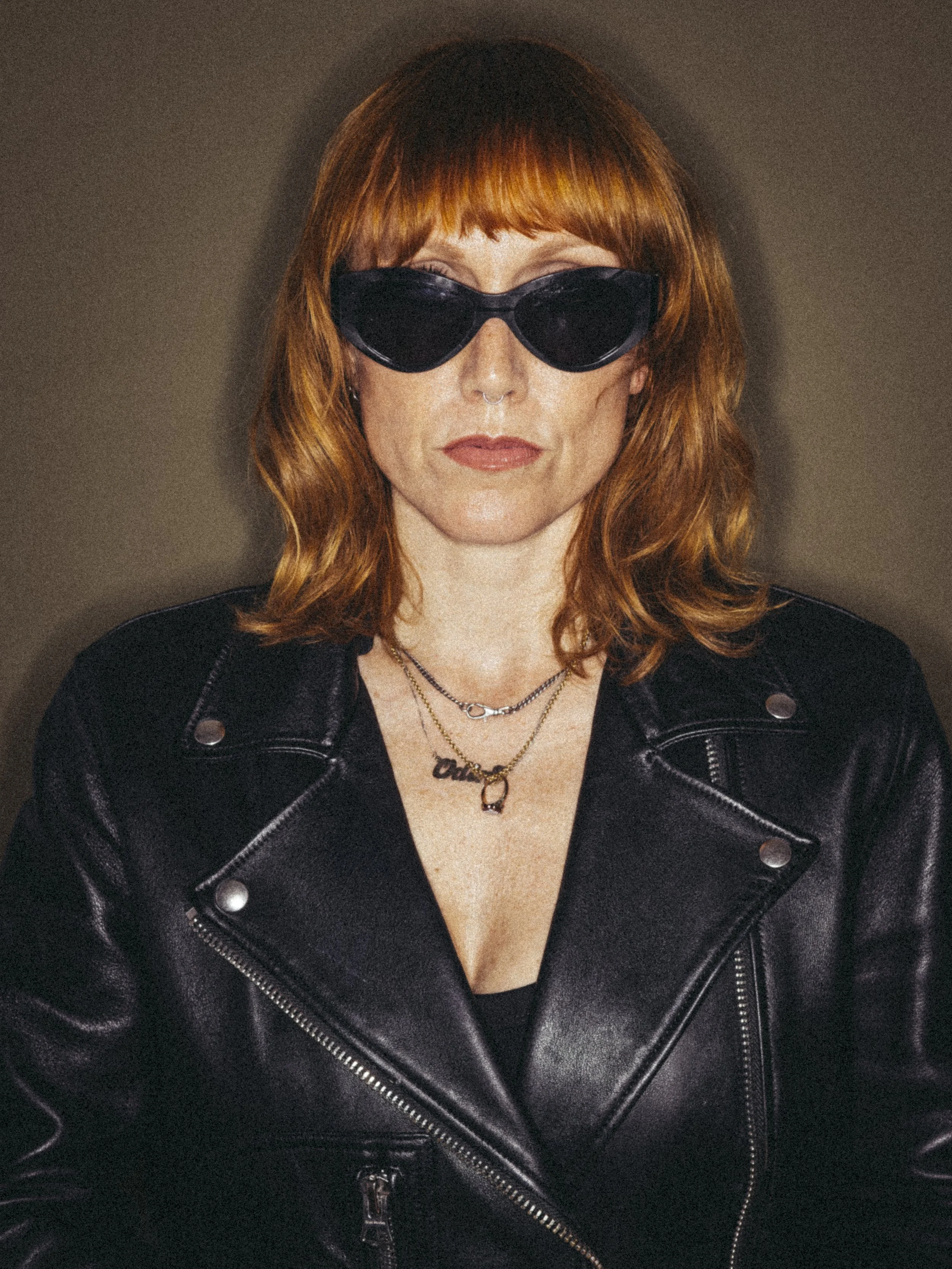 A woman with red hair wearing black sunglasses and a black leather jacket.