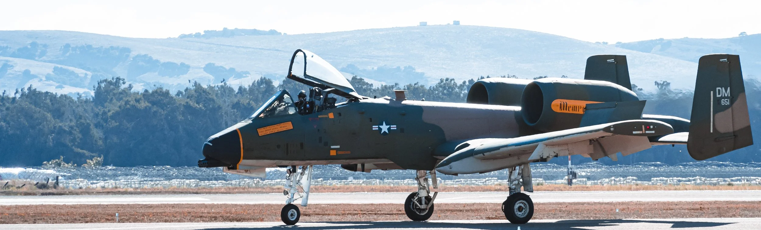 A military fighter jet, possibly an F-35, on the ground at an airstrip with mountains in the background.