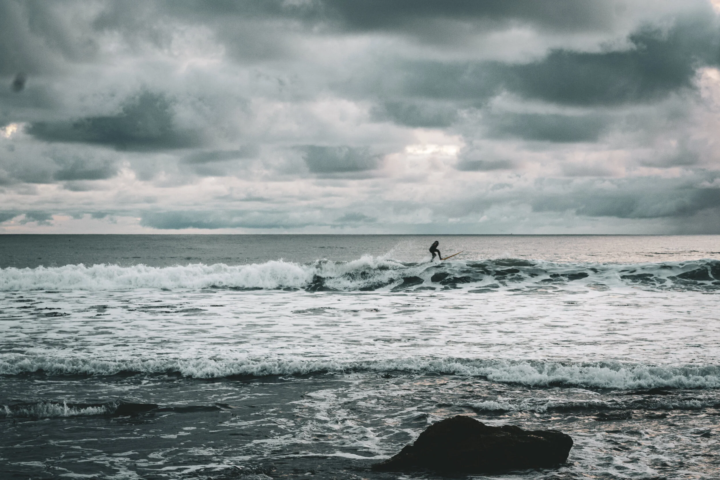 A person surfing on a wave in a cloudy ocean scene.