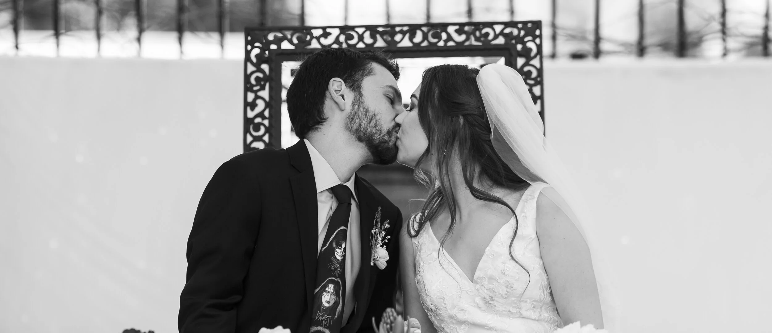Black and white photo of a bride and groom sharing a kiss during their wedding ceremony.