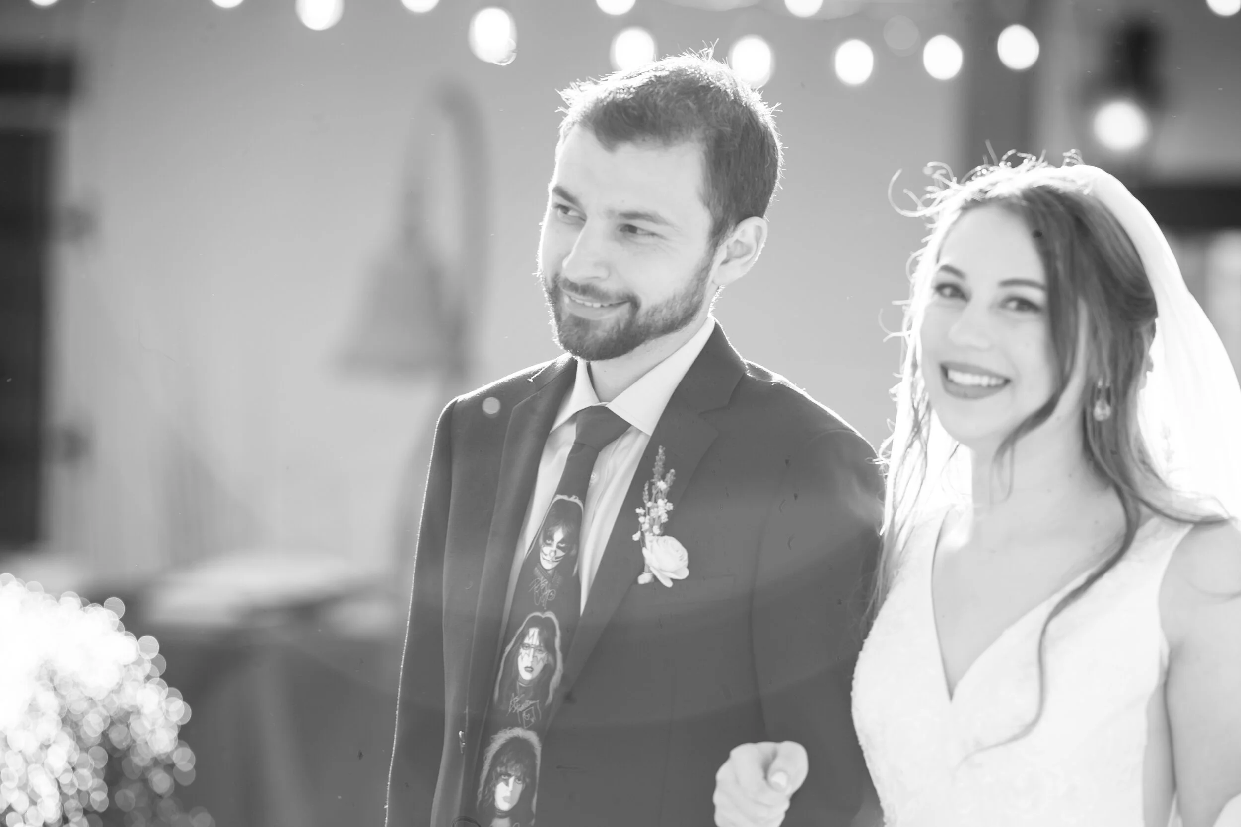 A black and white photo of a smiling man in a suit and tie standing next to a woman wearing a wedding dress and veil.
