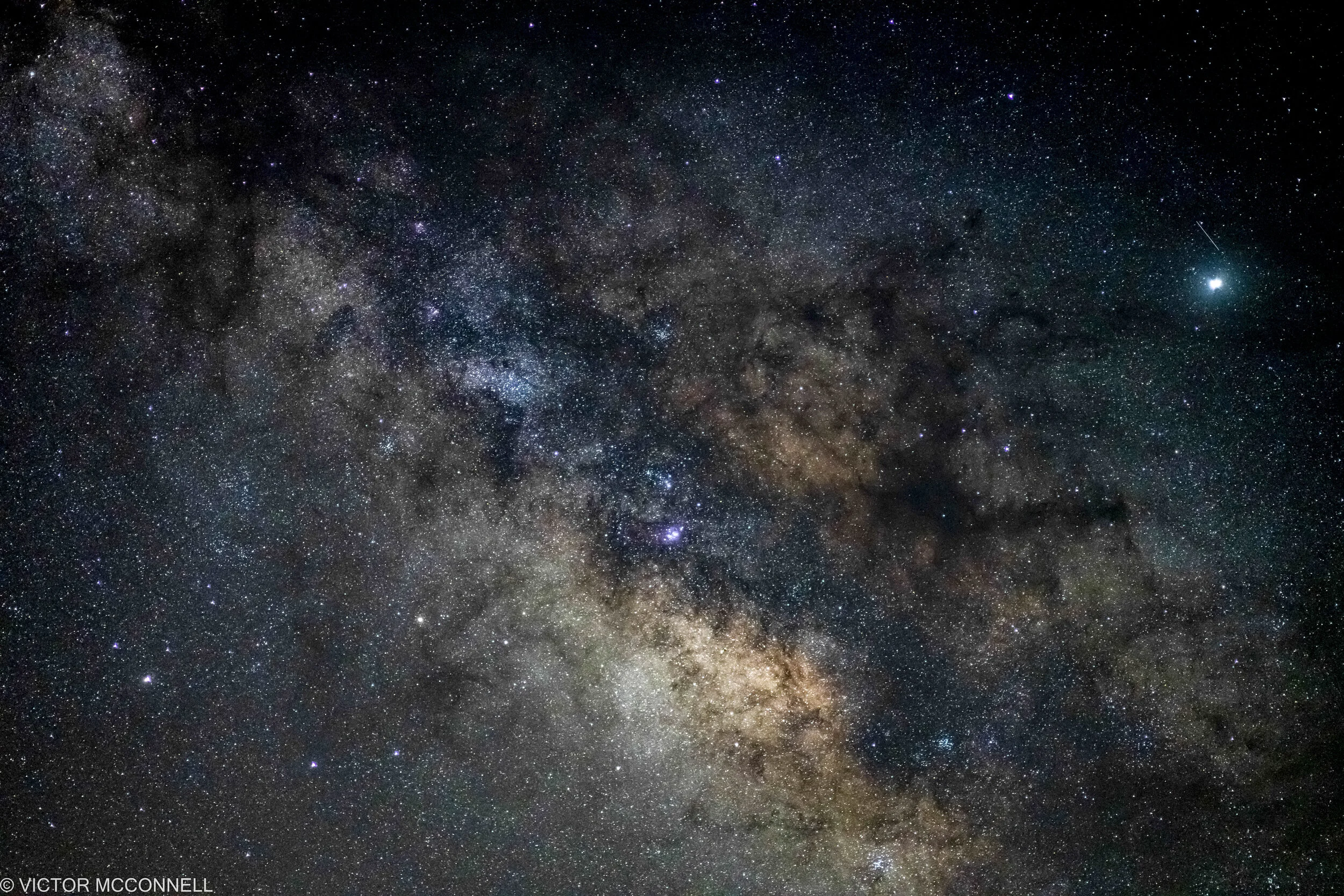 A wide view of the night sky showing the Milky Way galaxy with countless stars, gas clouds, and cosmic dust.