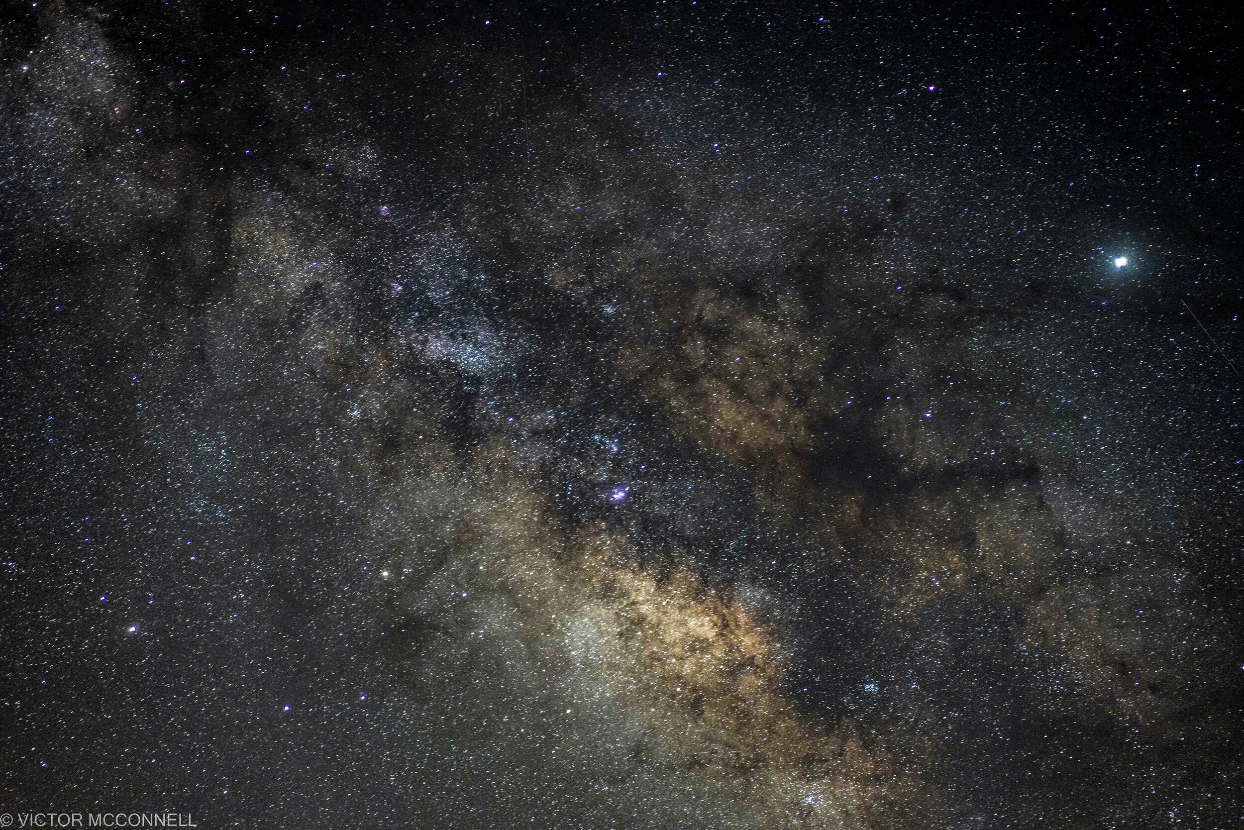 A view of the night sky filled with countless stars, including the Milky Way galaxy. The sky is dark, with a bright star or planet visible on the right side.