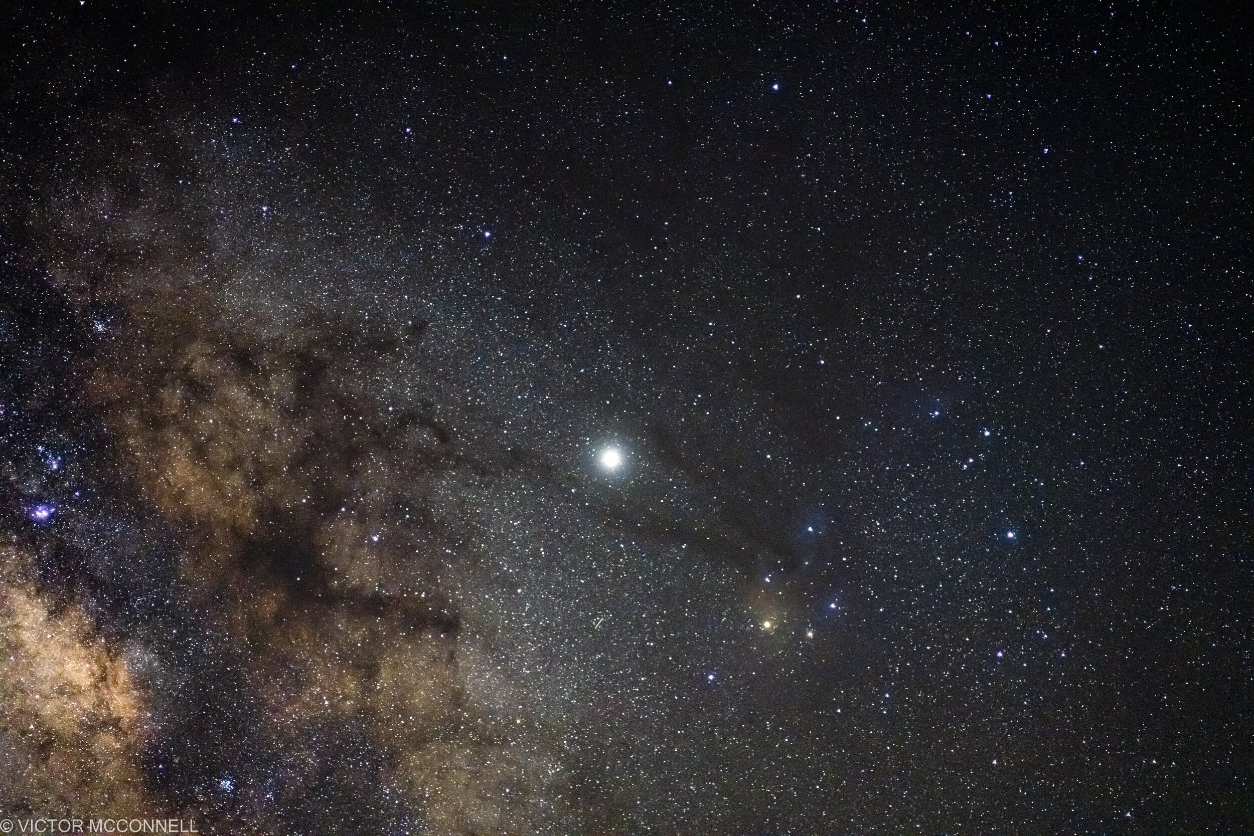 Starry night sky with numerous stars and a bright planet or star near the bottom.